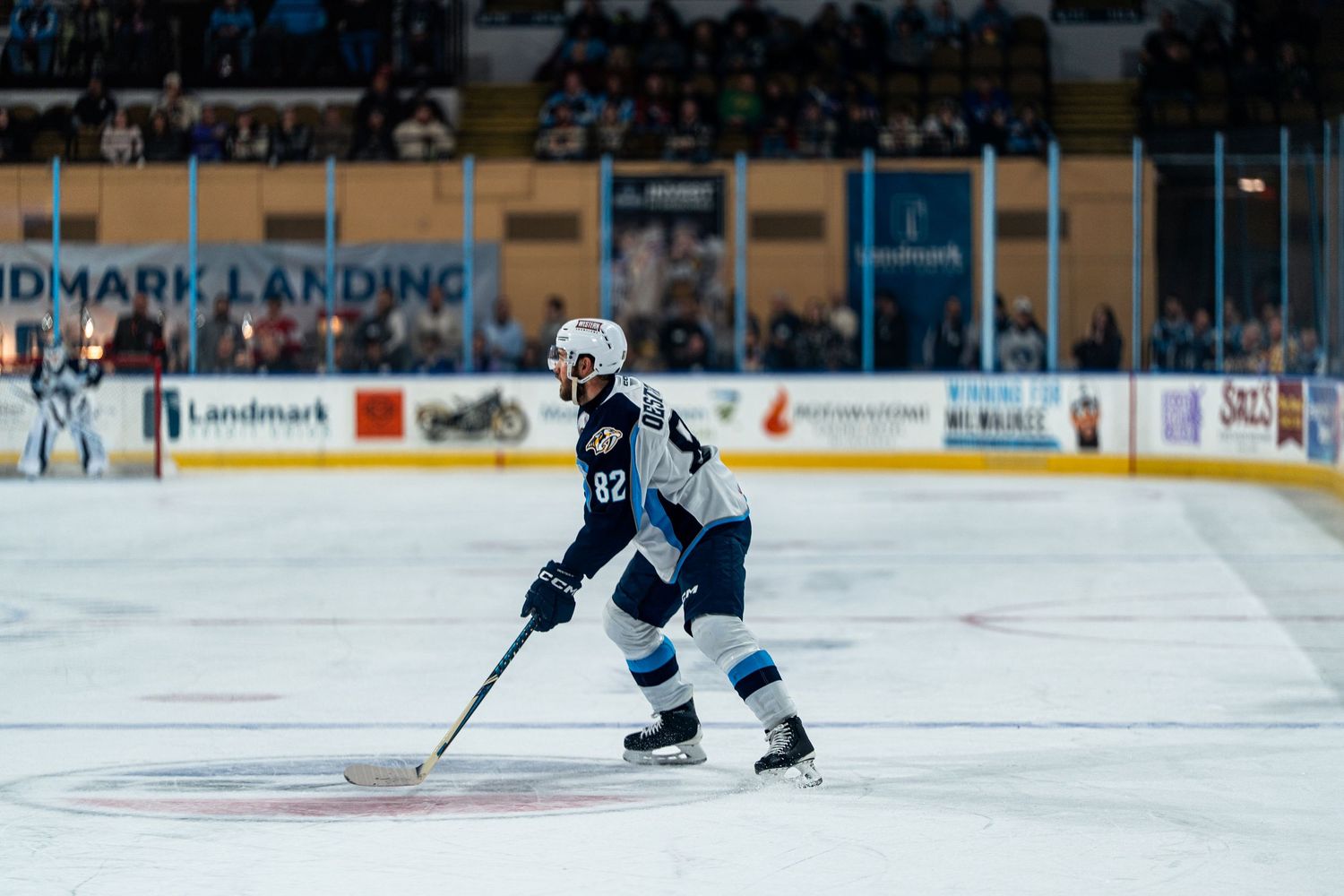 Wide shot of hockey players practicing on ice rink with crowd in background.
