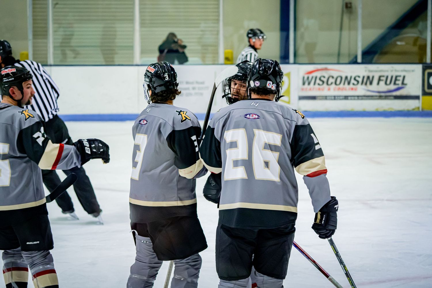 Youth hockey players in black and white jerseys compete during an ice hockey game at an indoor rink.