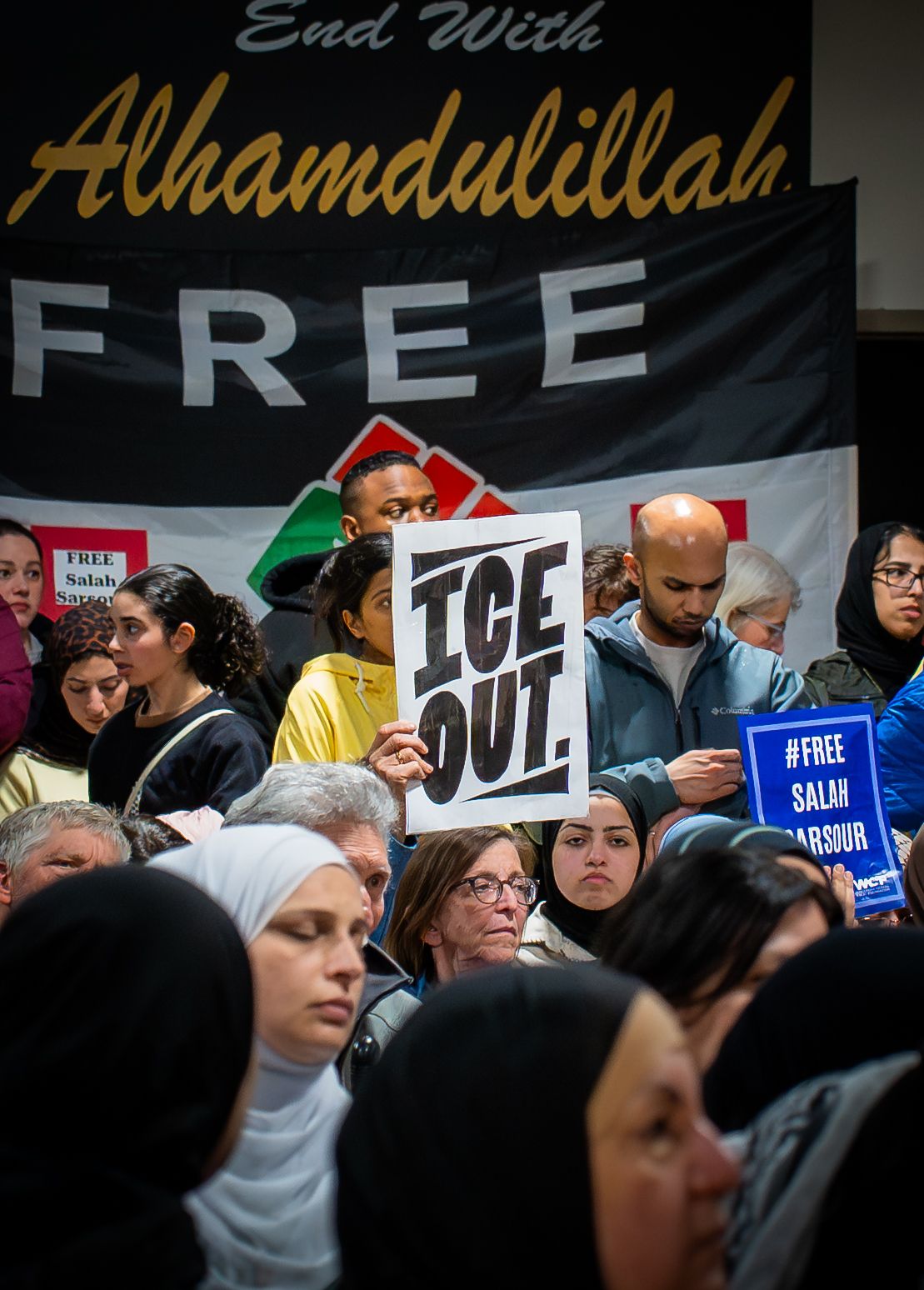 Protesters gather at rally holding 'ICE OUT' and 'Free Salah' signs, with Palestinian flags and banners visible in crowd.