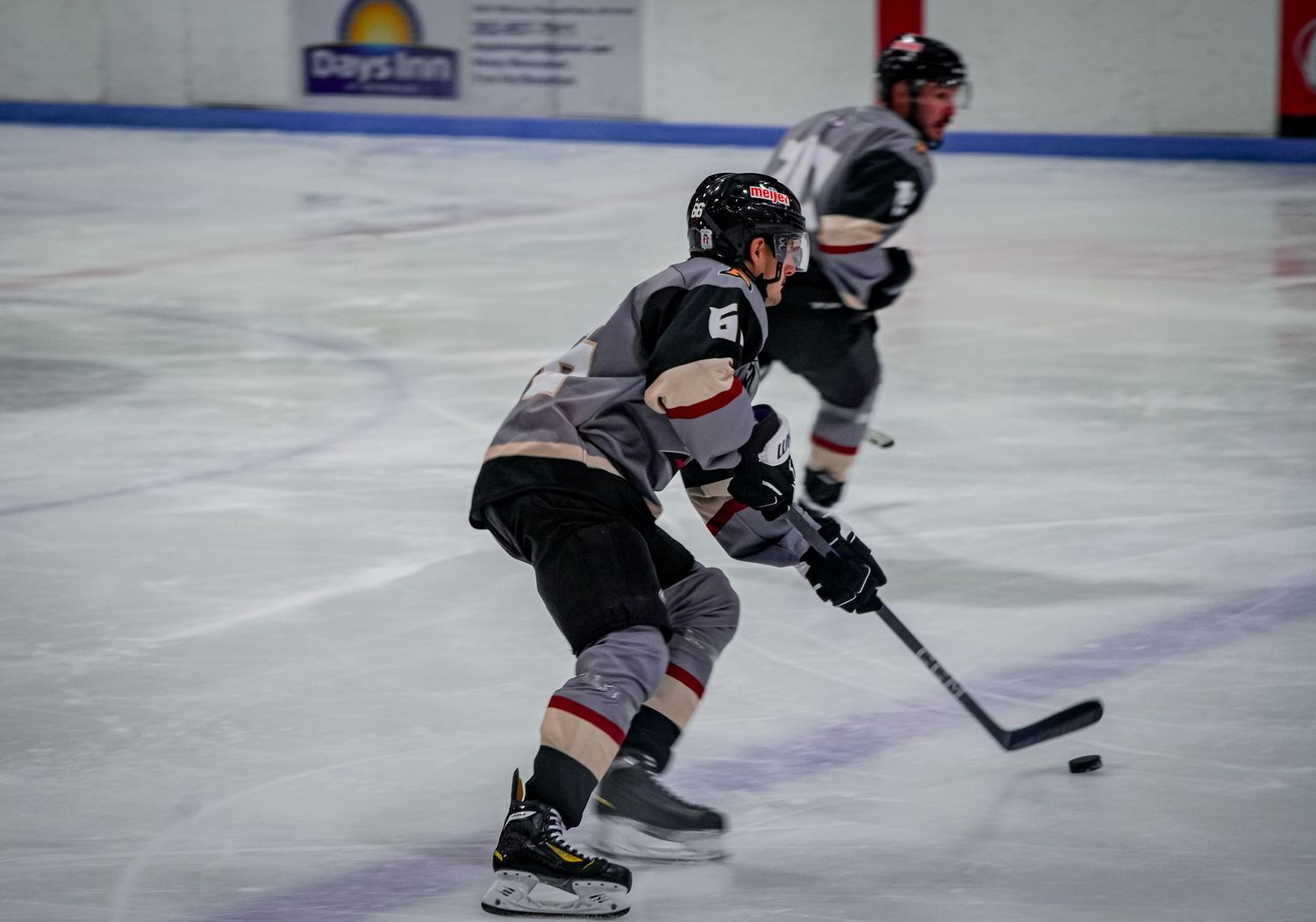 Hockey player in gray jersey handles puck while skating on ice during competitive match.