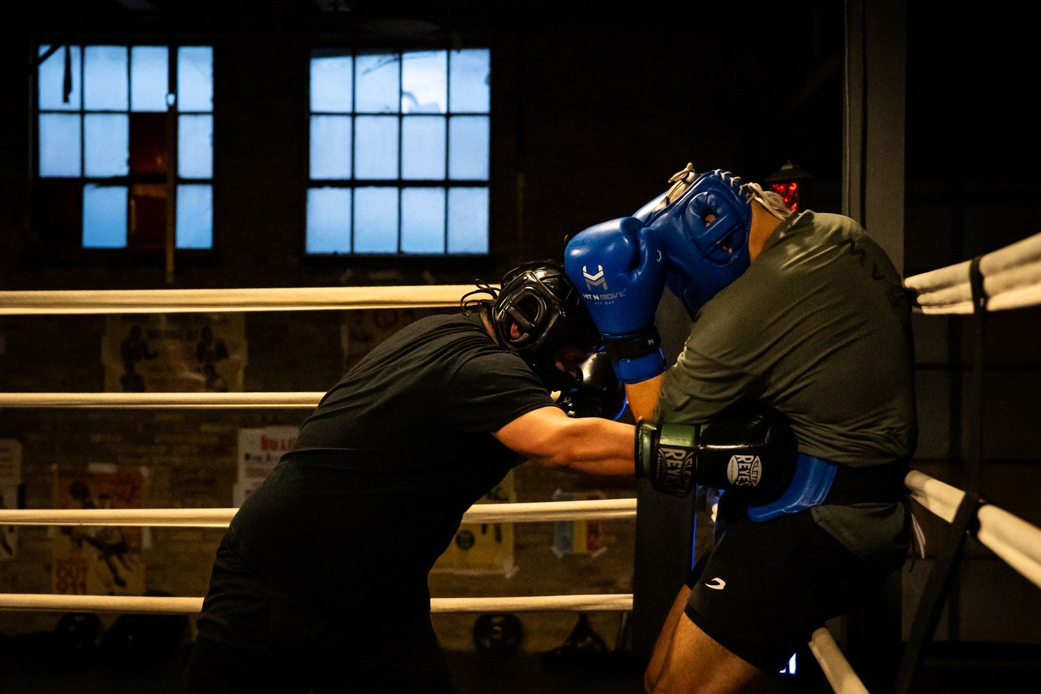 Two athletes engage in boxing practice wearing protective headgear and gloves.