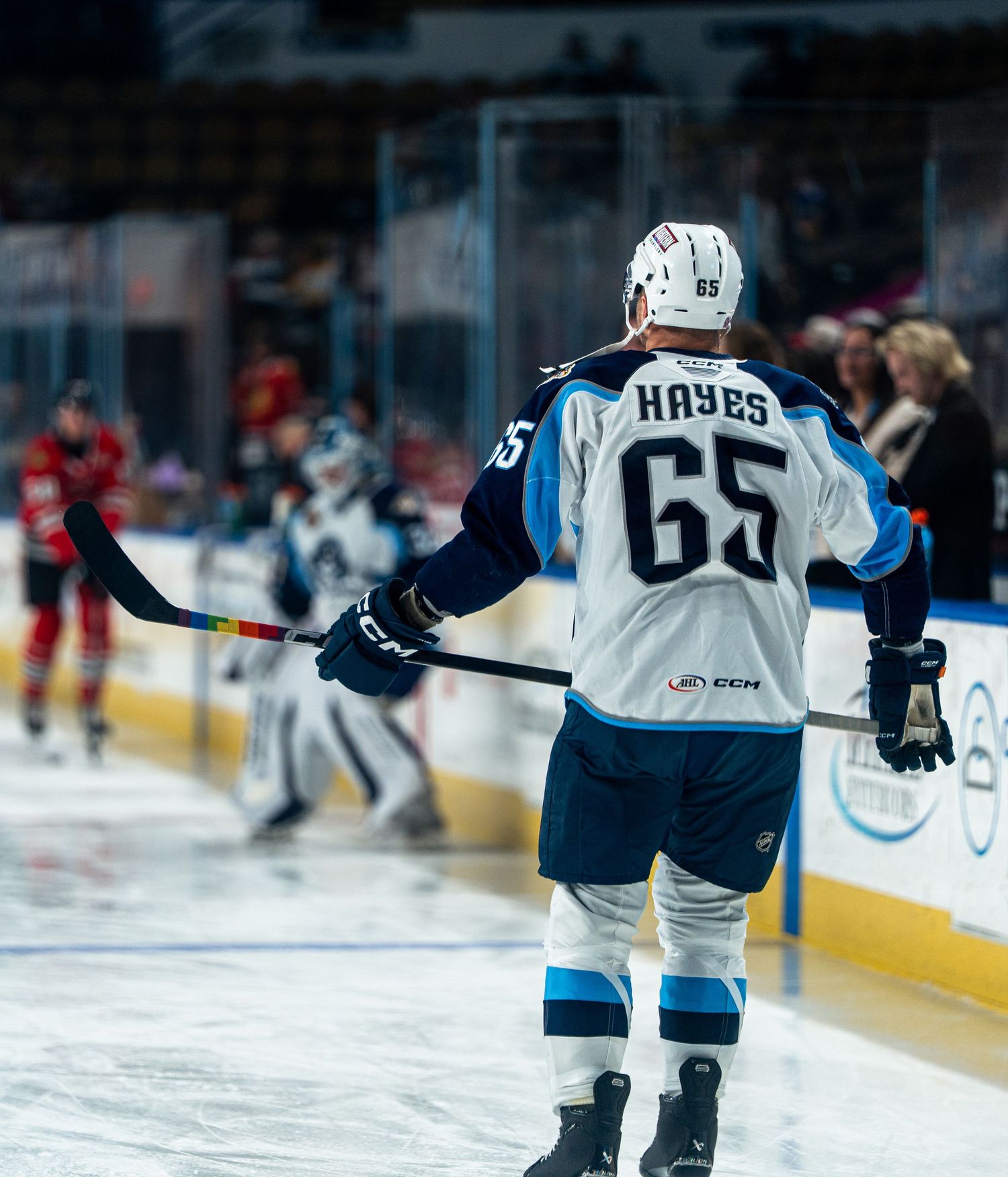 Hockey players glide across the ice during a competitive game with sponsors visible on the rink boards.