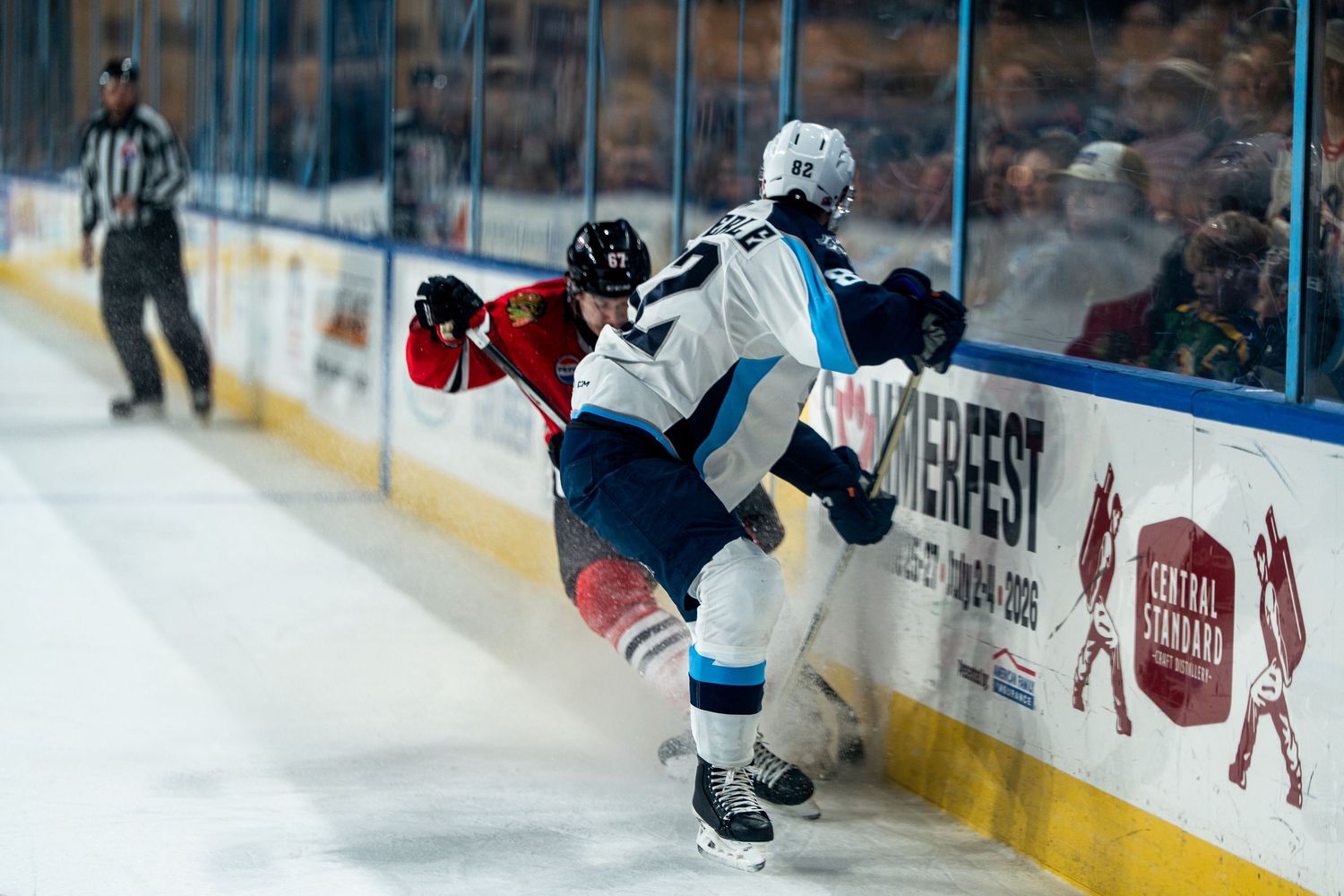 Hockey players engage in physical play along the boards during game action.