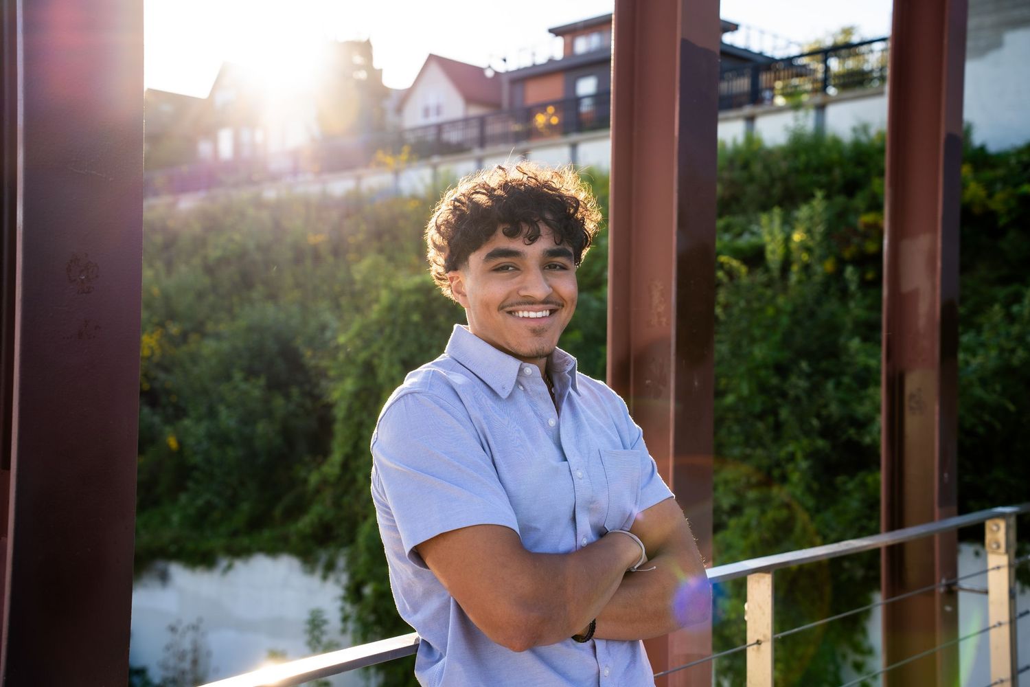 Person in light blue shirt smiling outdoors during golden hour lighting.