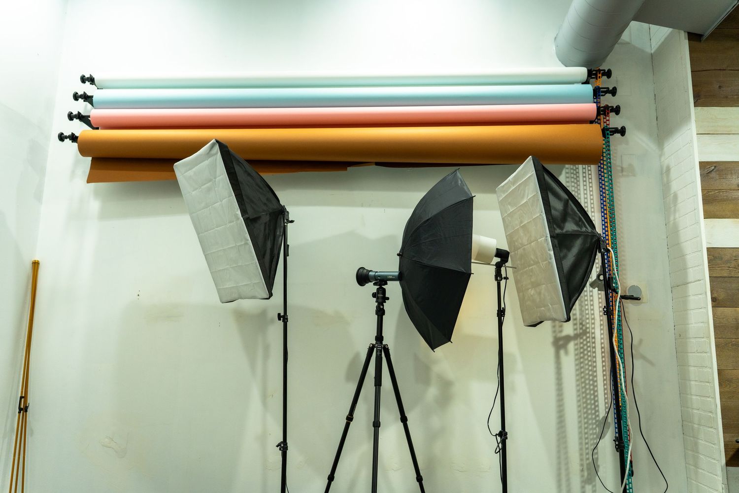 Photography studio equipment setup with lighting umbrellas, tripod and backdrop rolls mounted on the wall.