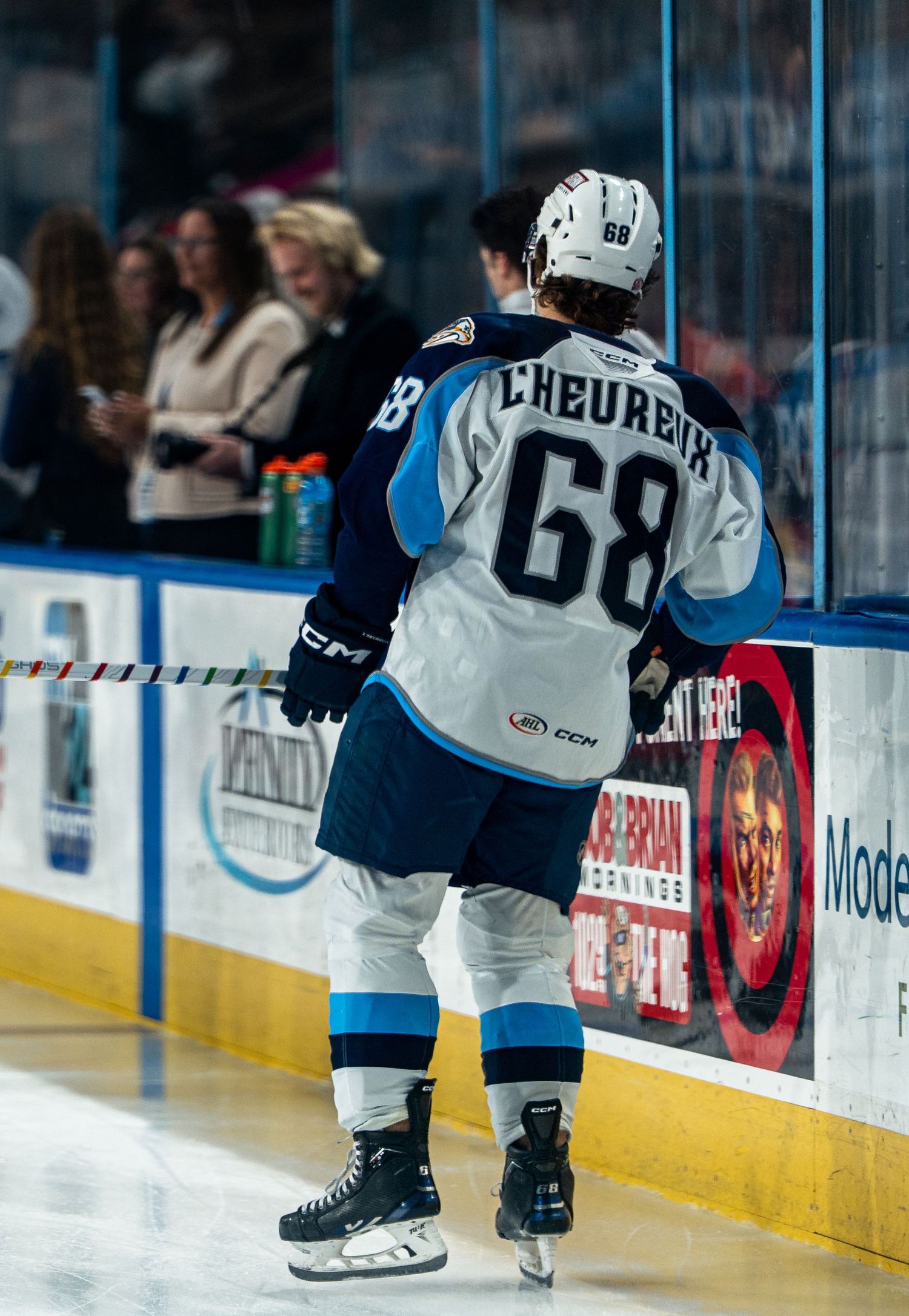 Ice hockey players in blue and white uniforms skate along the boards during a competitive match.