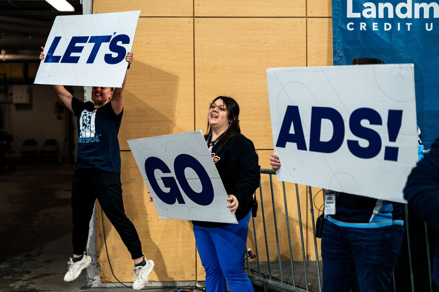 Fans hold up supportive signs at a hockey game against a yellow wall background.