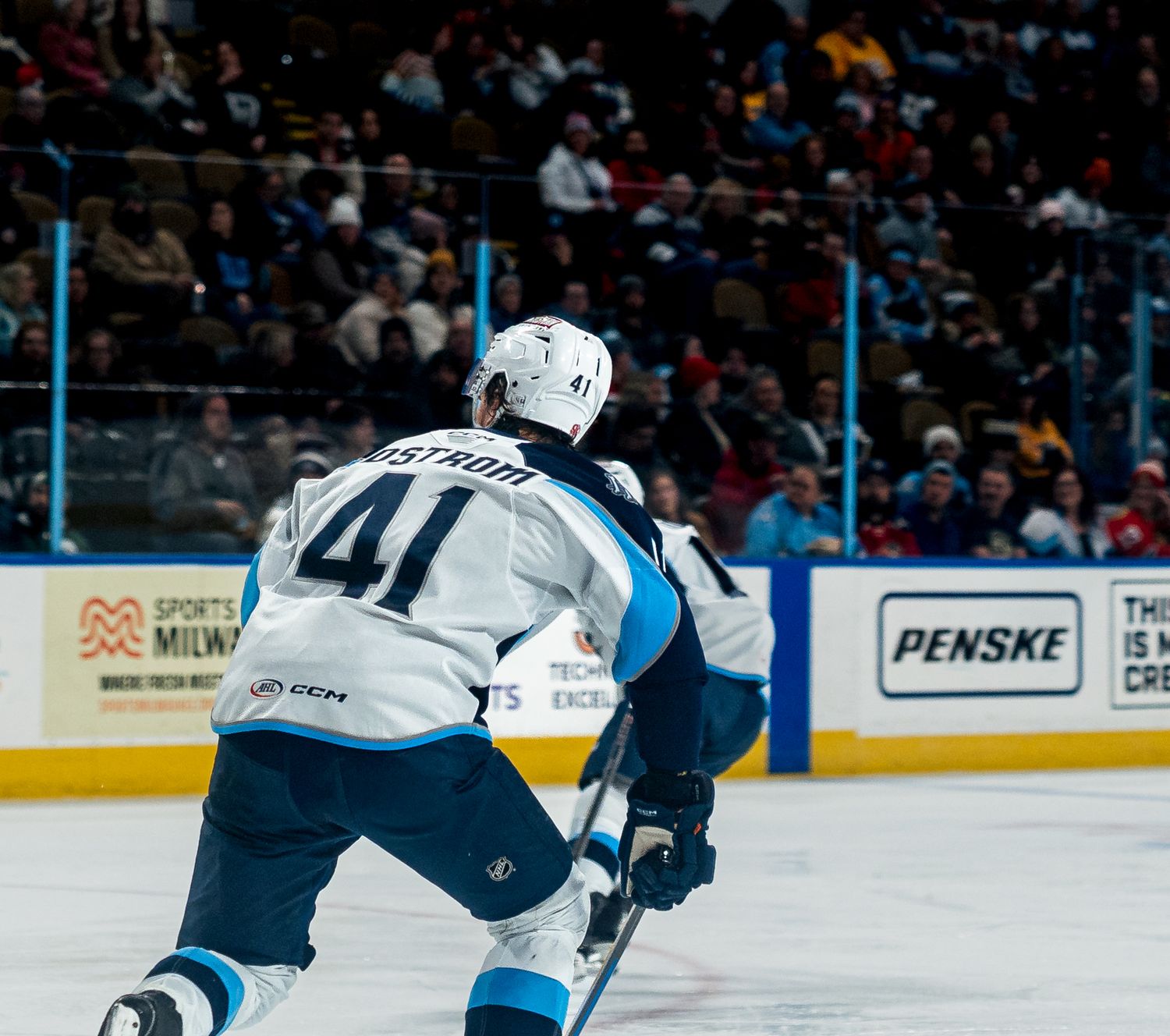 Hockey players in white and blue uniforms skate during competitive play.