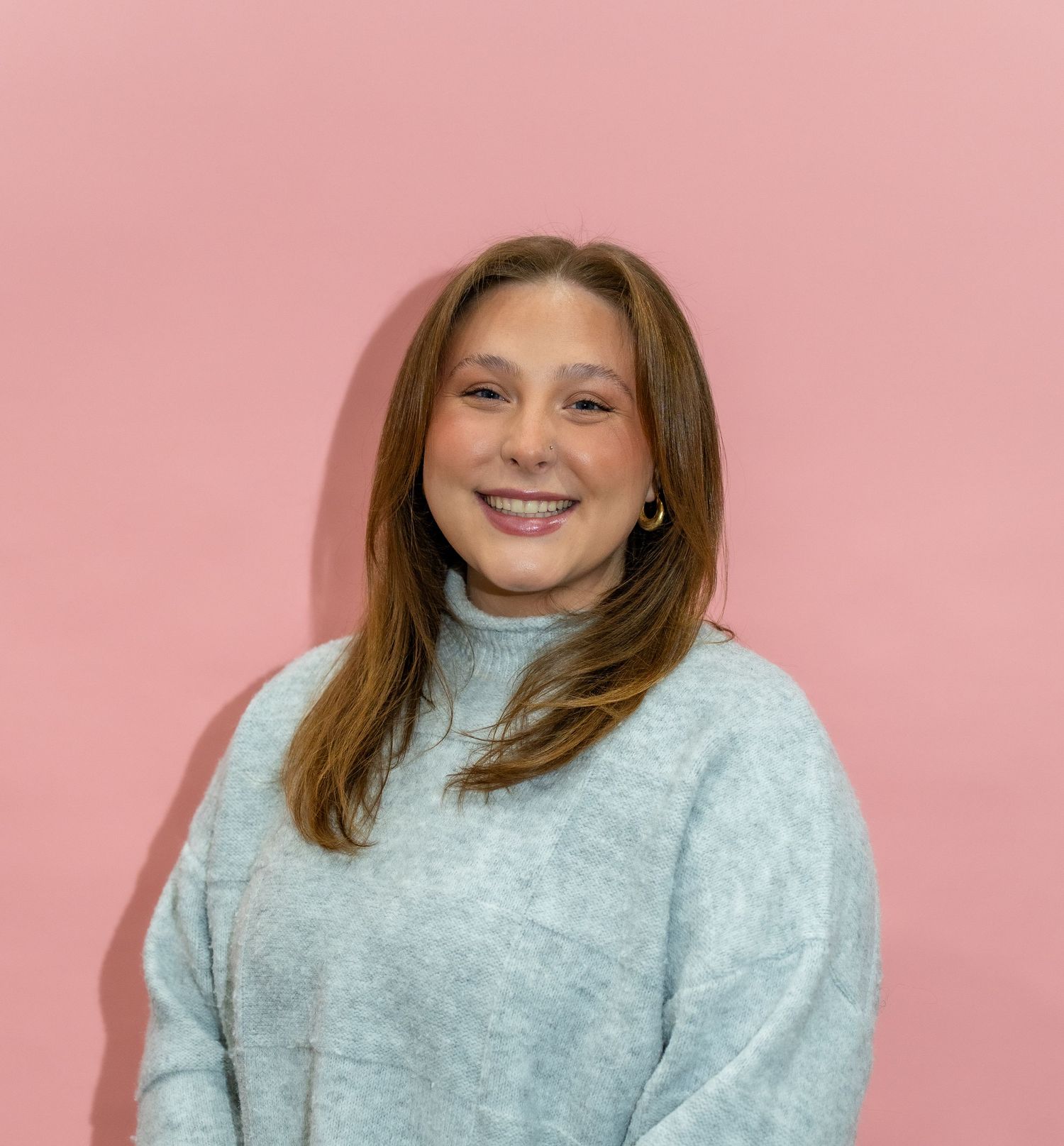 Person wearing a light blue turtleneck sweater poses against a pink background in a photo series.