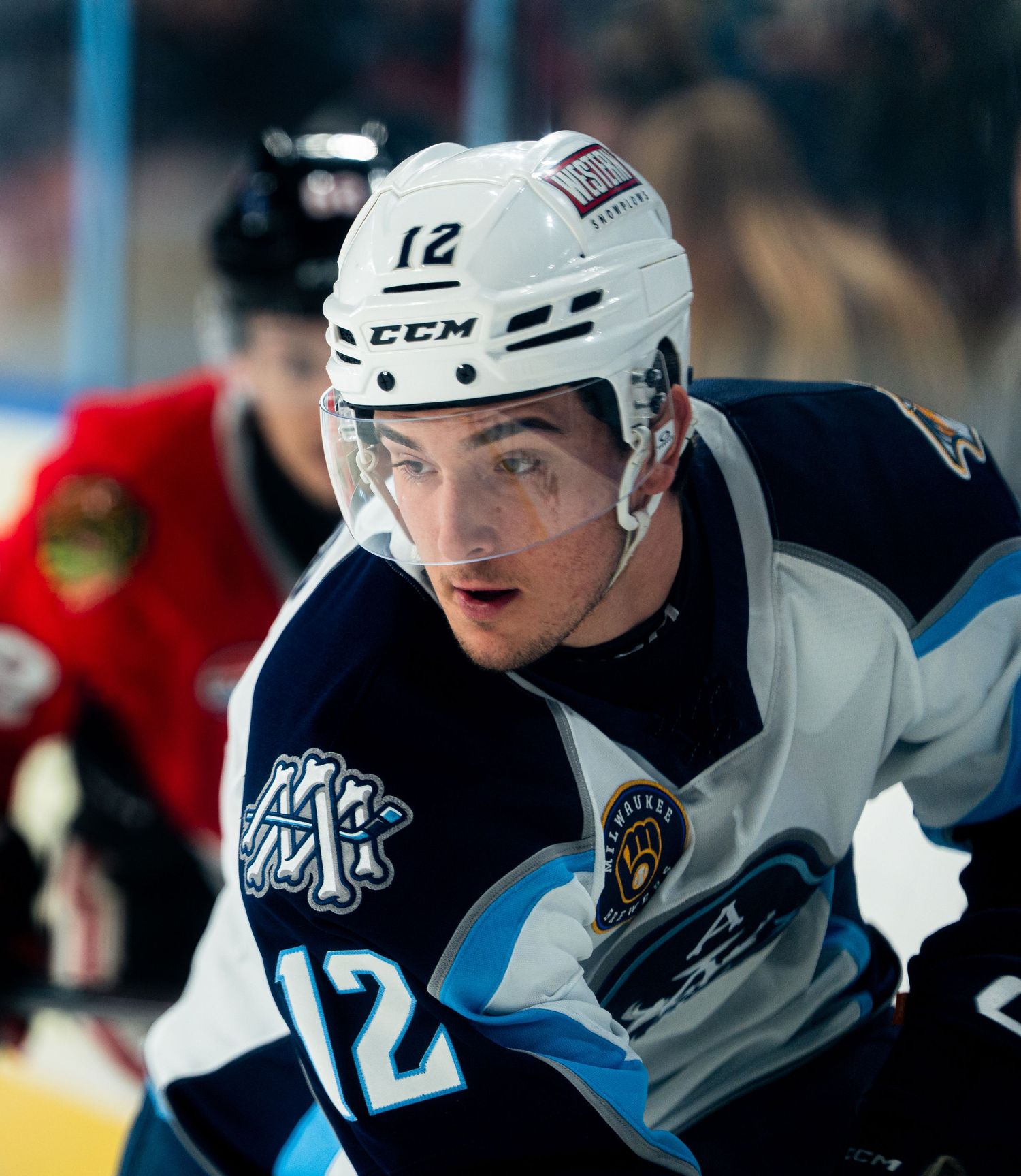 Hockey player in white jersey number 12 moves across the ice during gameplay.