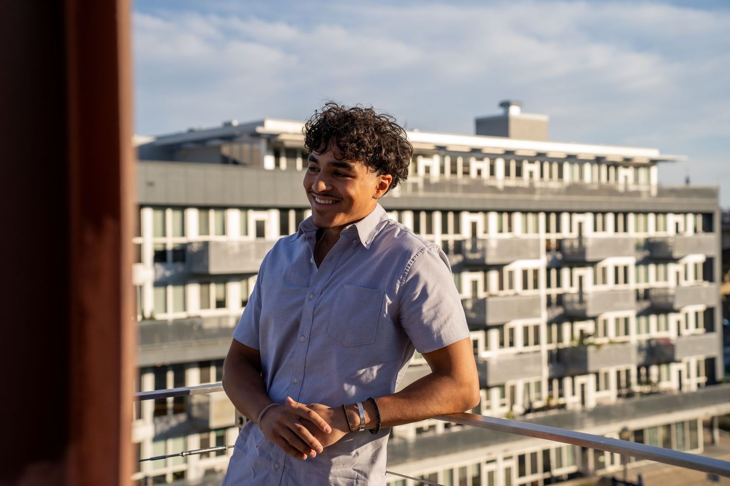 Person in blue shirt looking at phone on balcony with buildings in background.