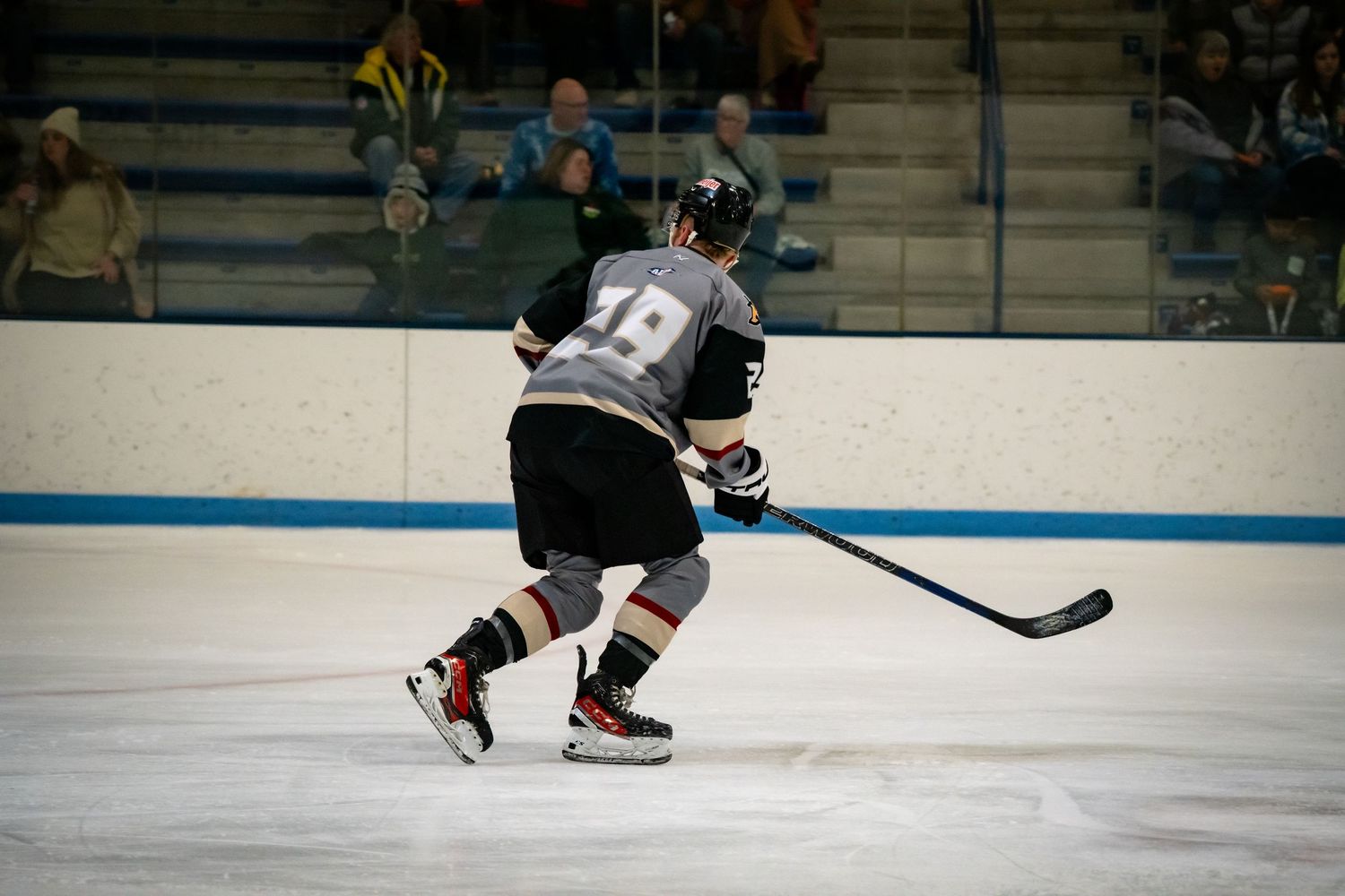 Hockey players in dark uniforms chase after the puck on an indoor ice rink.