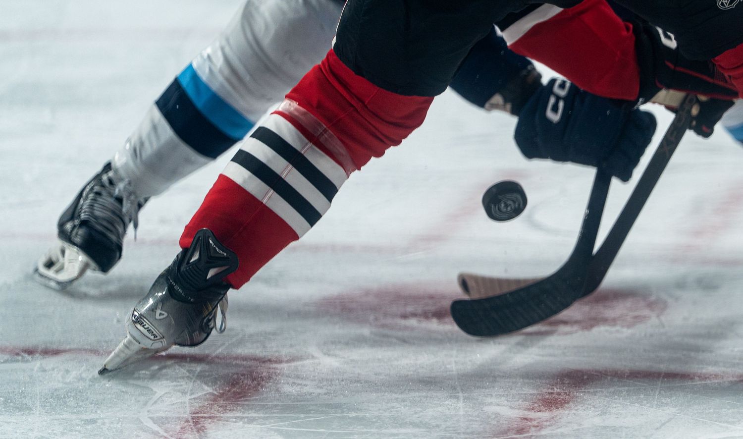 Close-up of hockey skates and stick during face-off at ice level.