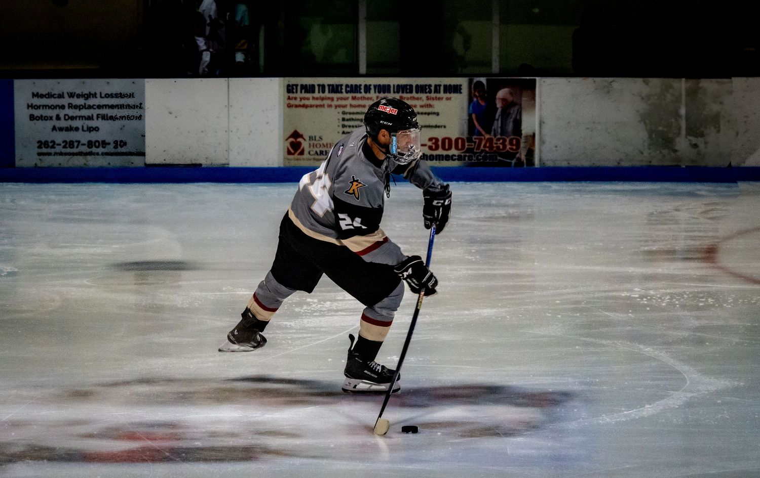 Hockey players skate on ice during an intense game at an indoor rink with advertisements visible on the boards.