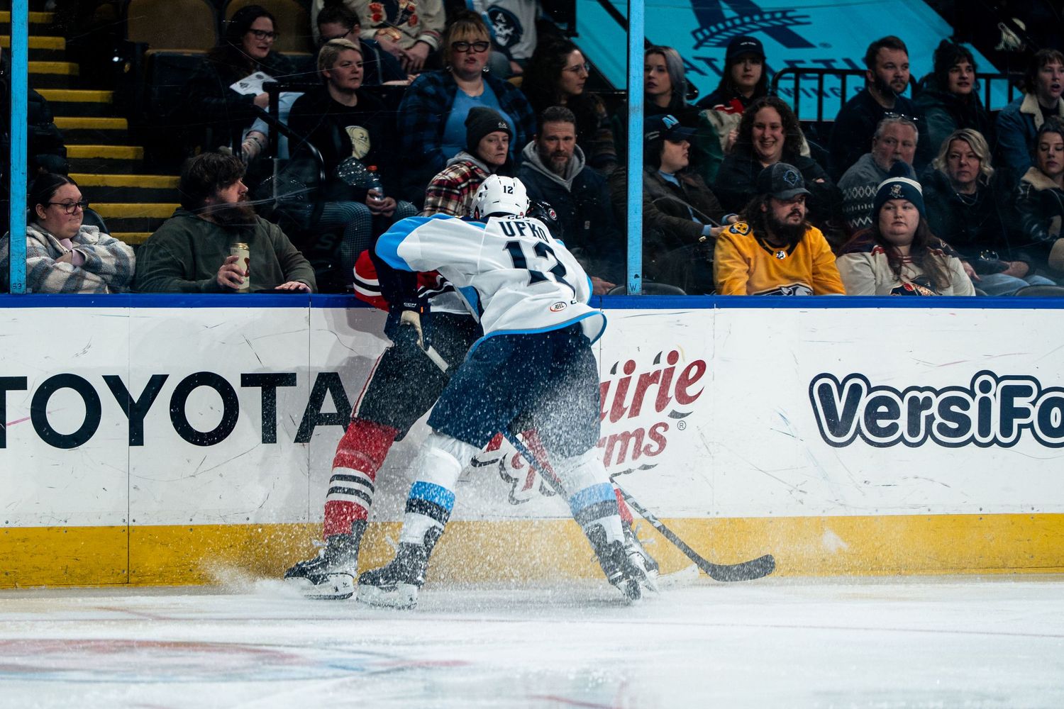 Hockey players from opposing teams compete for the puck along the boards.