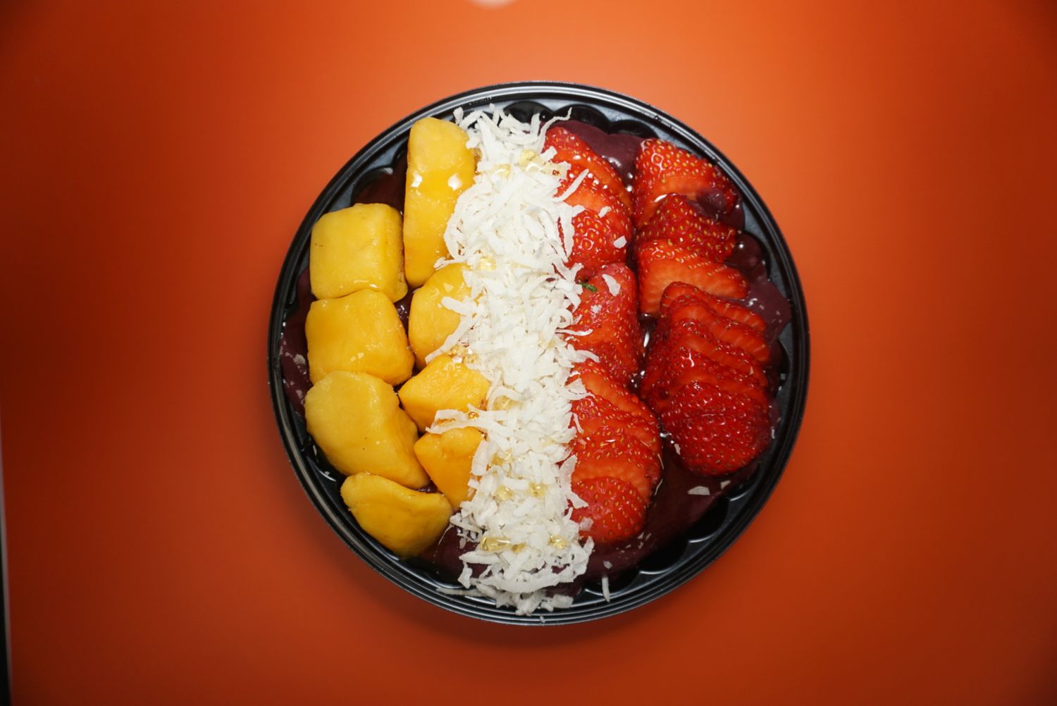 Colorful fruit bowl with mango, shredded coconut and strawberries on orange background.