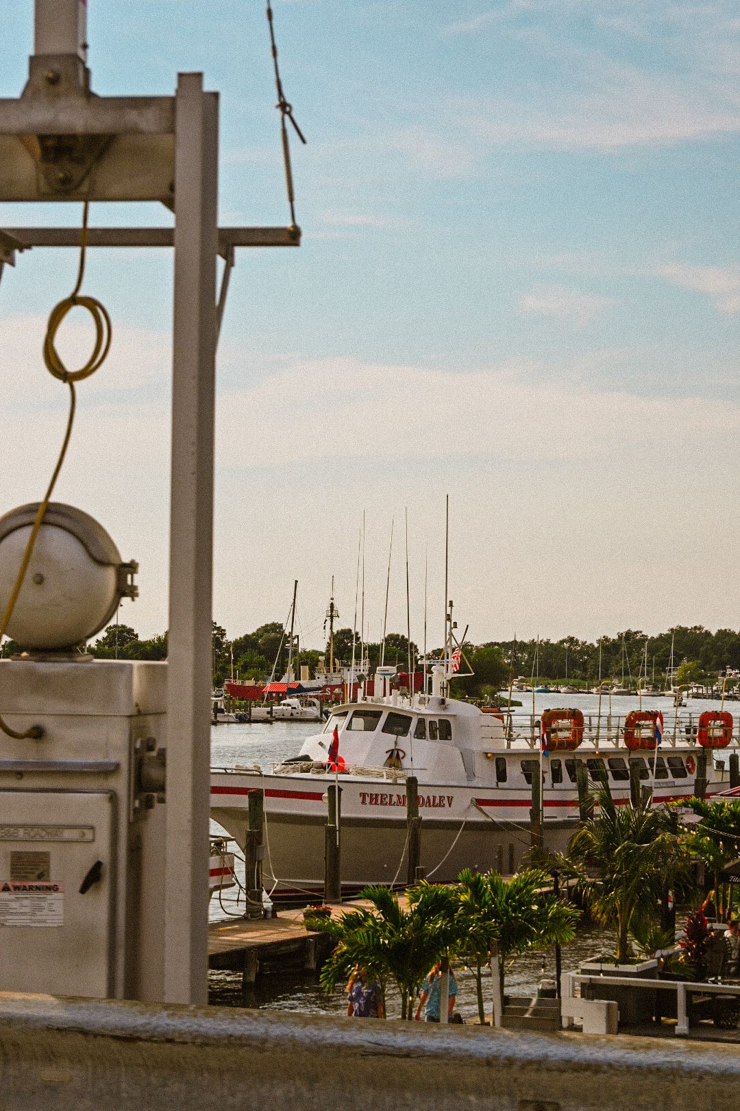 Marina dock with boats and yachts moored under a bright blue sky.