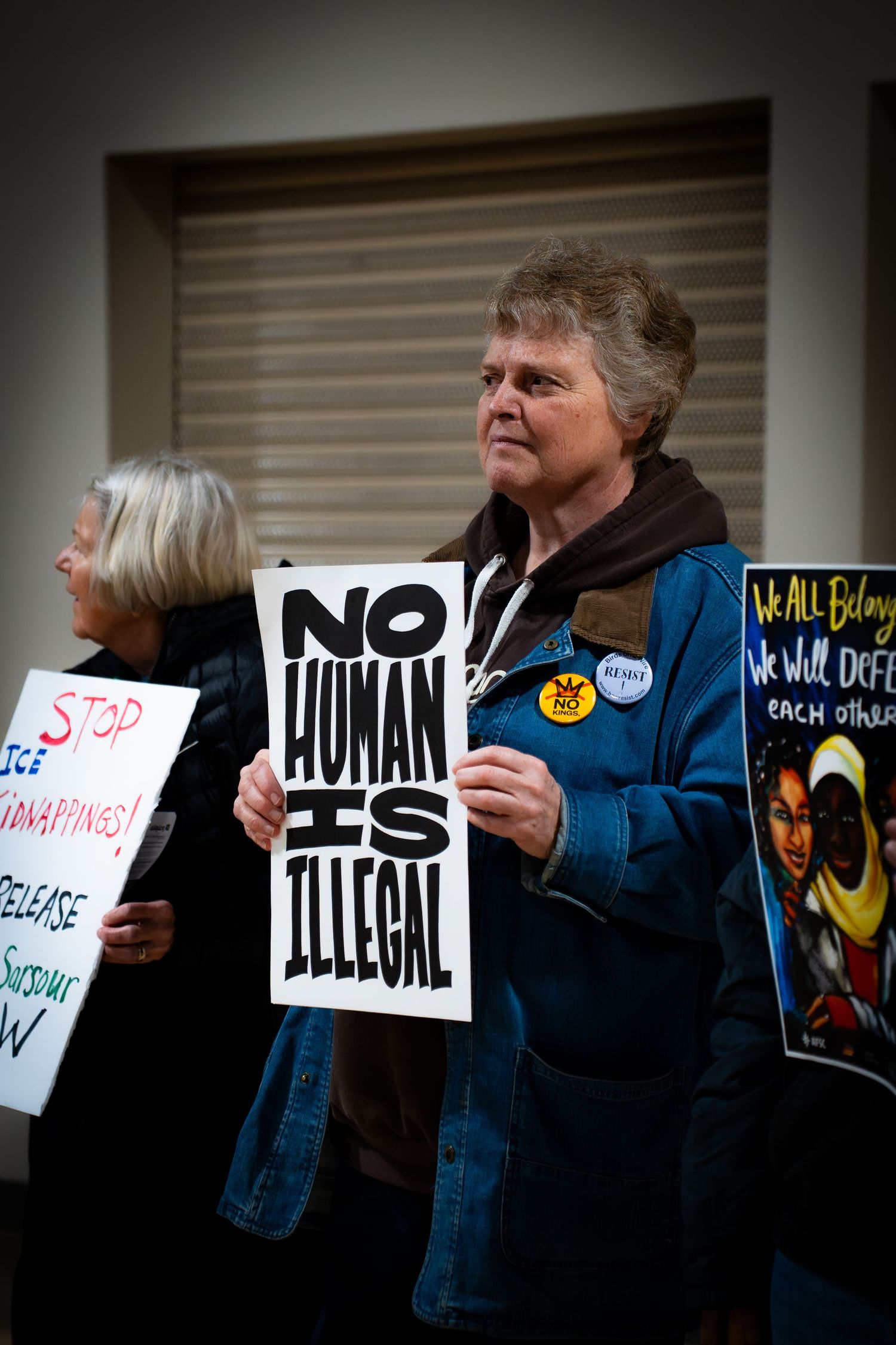 Woman holding No Human Is Illegal protest sign at immigration rally with other demonstrators holding signs.