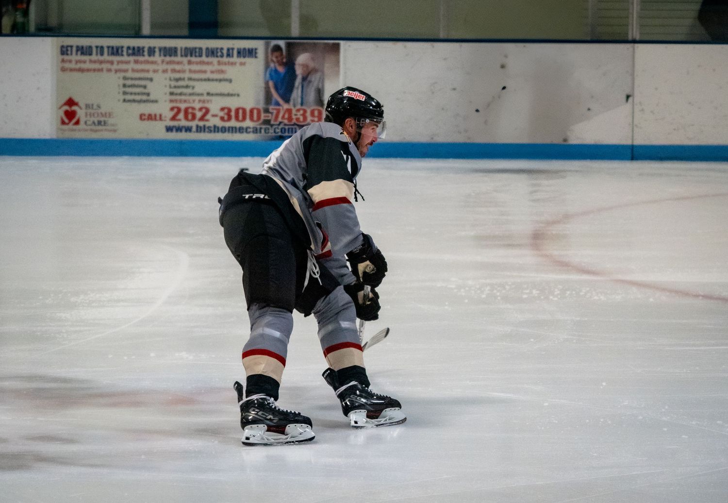 Hockey player in black and white uniform kneels on ice rink during practice session.