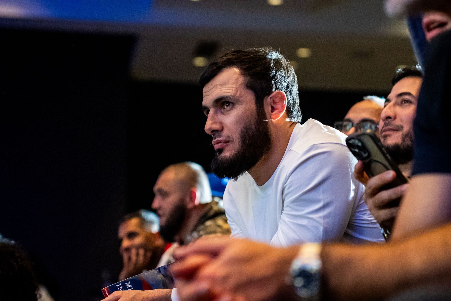 People in a dimly lit venue looking attentively at something off-camera during an event.