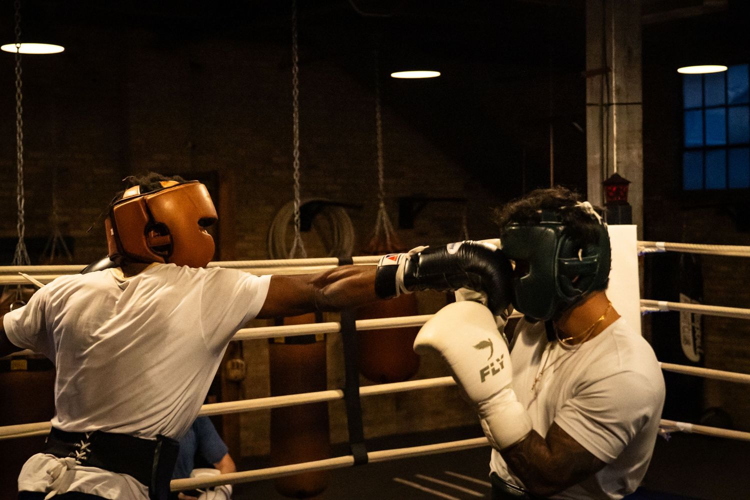 Boxers practicing defensive moves against the ropes in a dark gym setting.