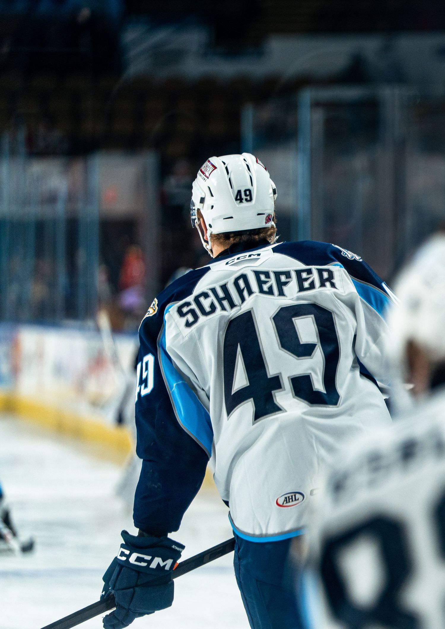 Hockey players in white and blue jerseys skate on ice during a professional game.