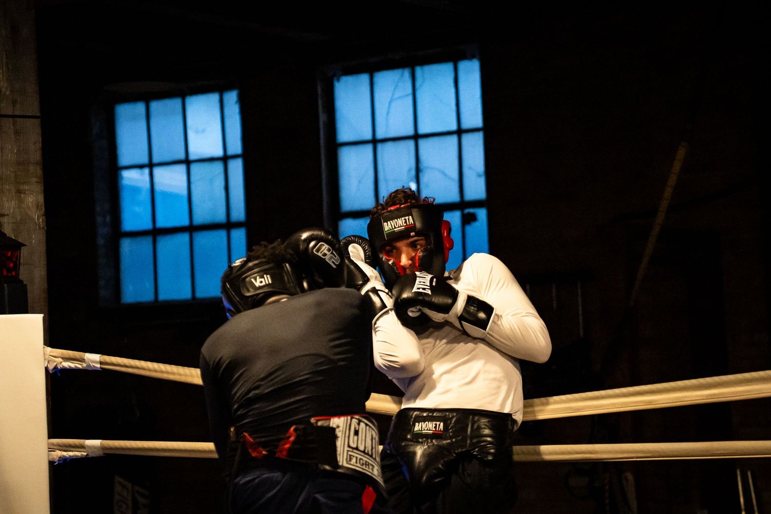 Sparring session between two boxers in protective gear within a traditional boxing ring.