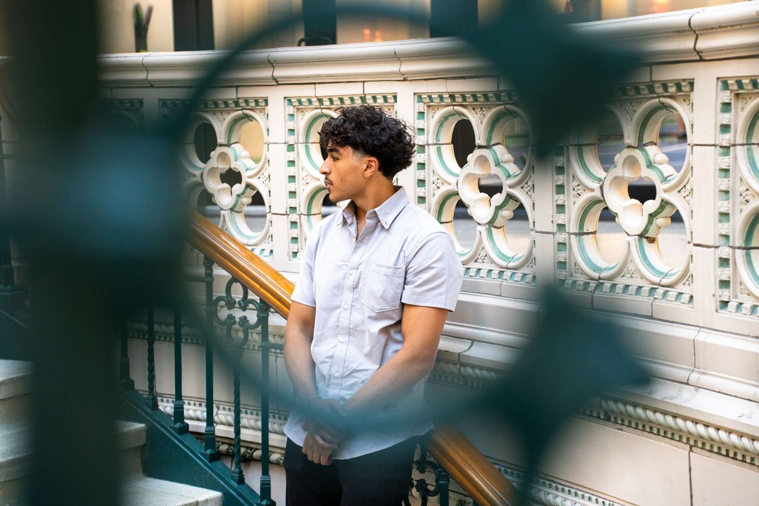 Person in blue shirt using phone against ornate white architectural details.