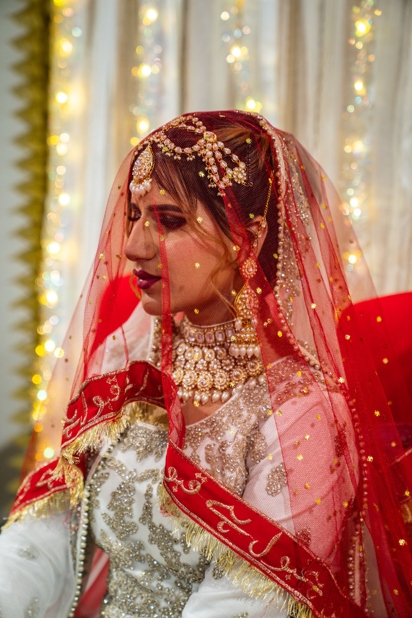 Detailed view of ornate bridal wear with red veils and elaborate jewelry.