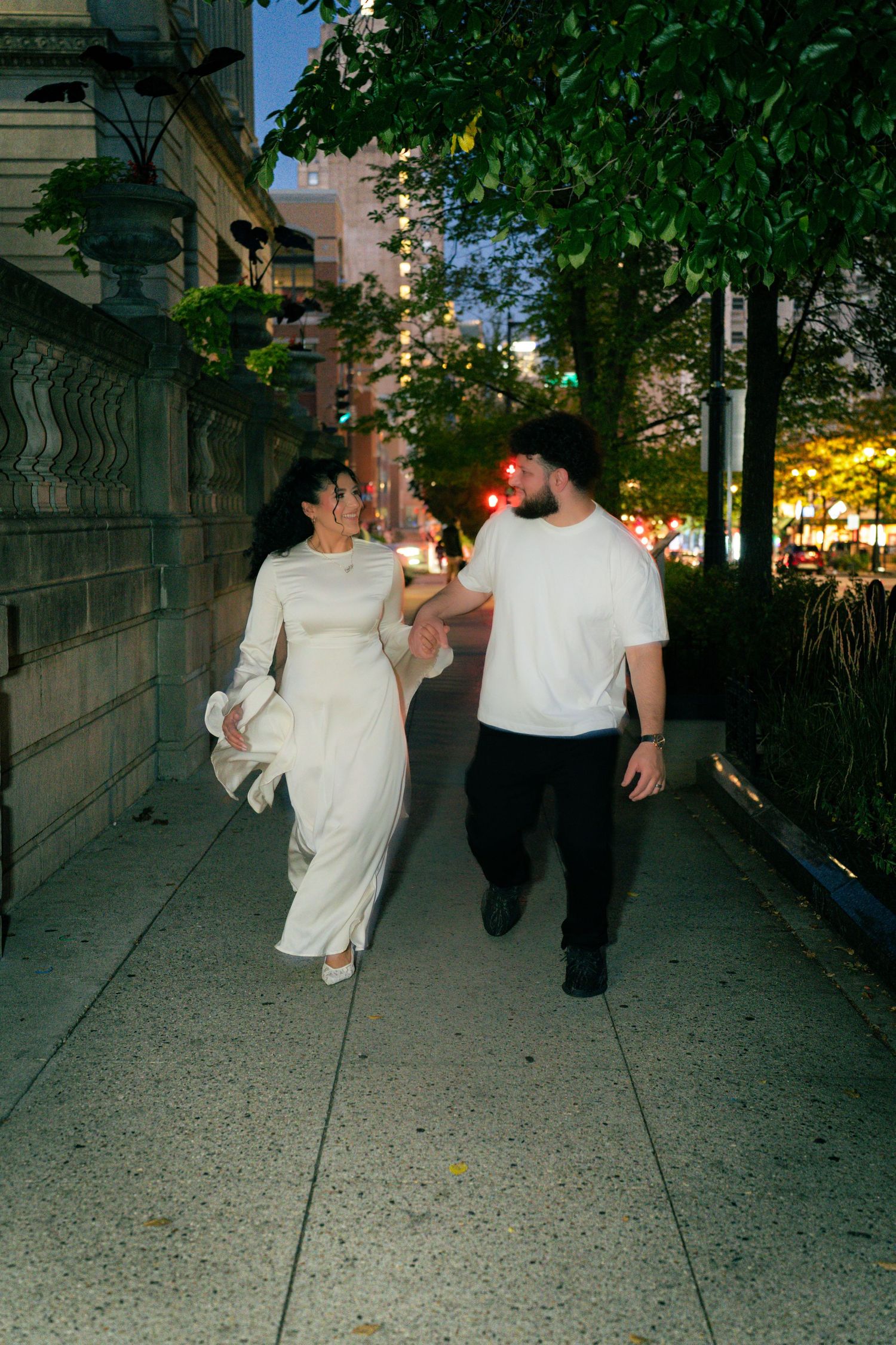 Couple running playfully down a city sidewalk at dusk.