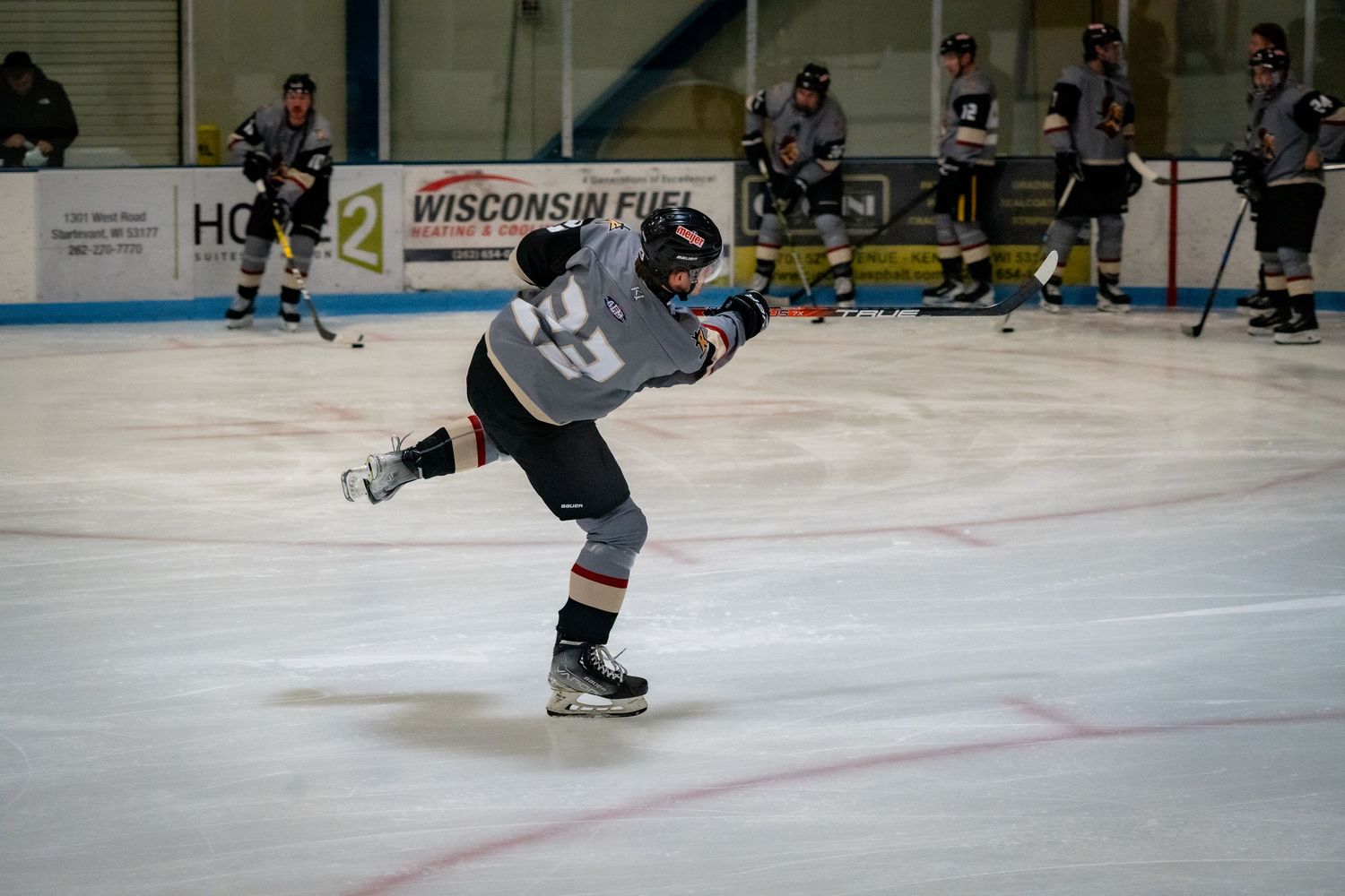 Ice hockey players skate across the rink during a competitive game with advertising boards visible.