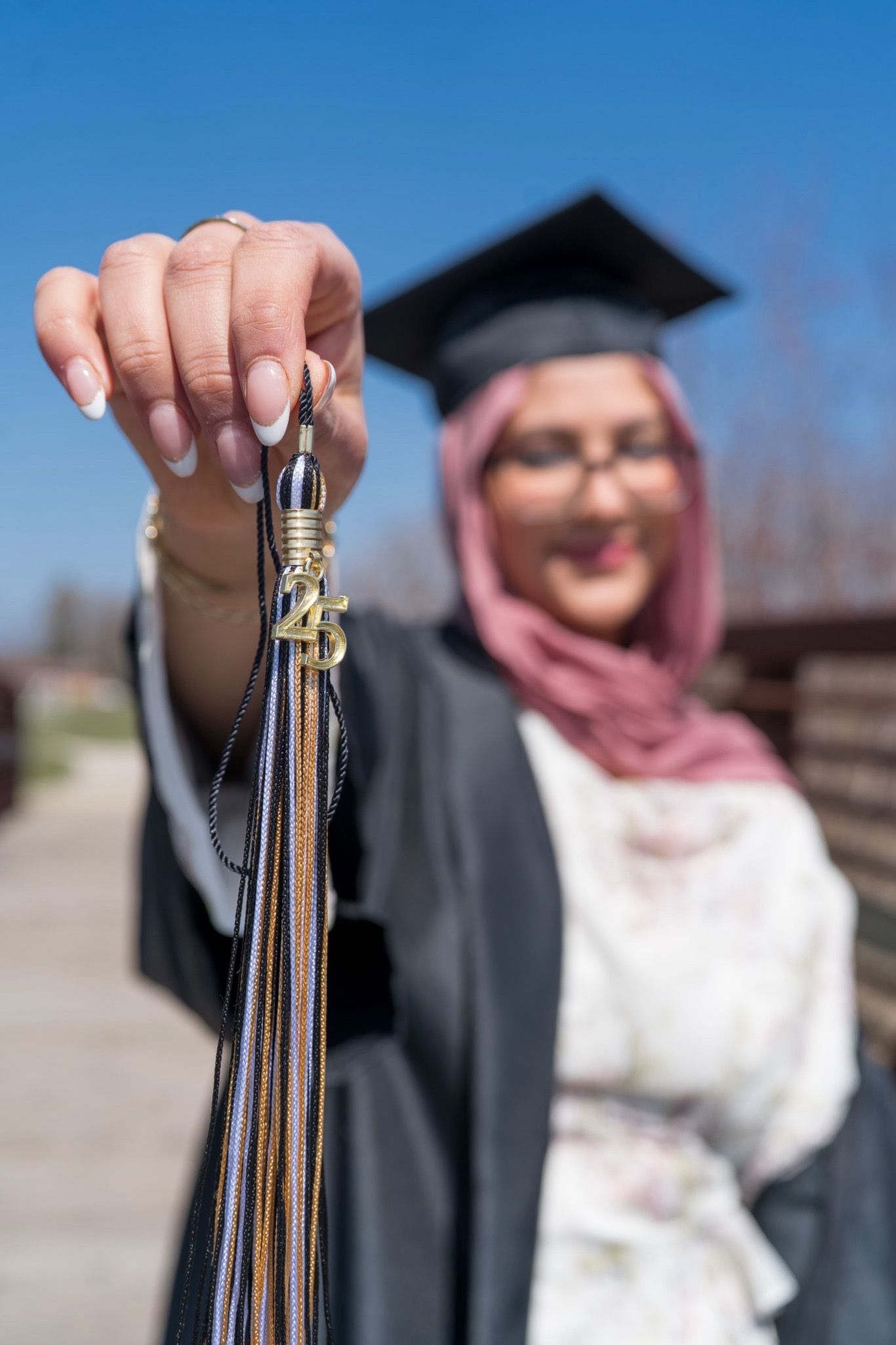 Graduate holding up their diploma tassels against bright blue sky.
