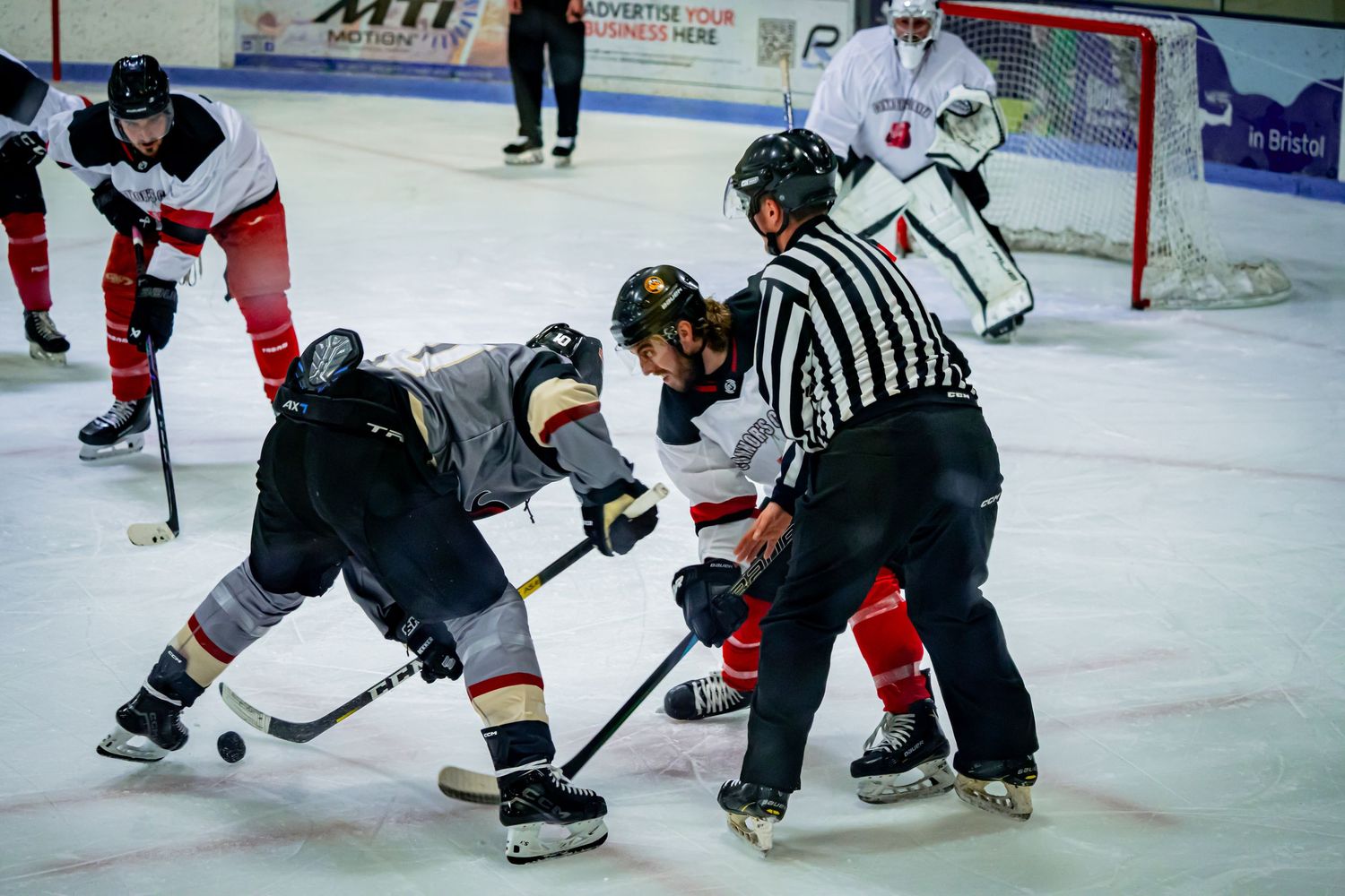 Ice hockey game action with players battling for puck near referee.