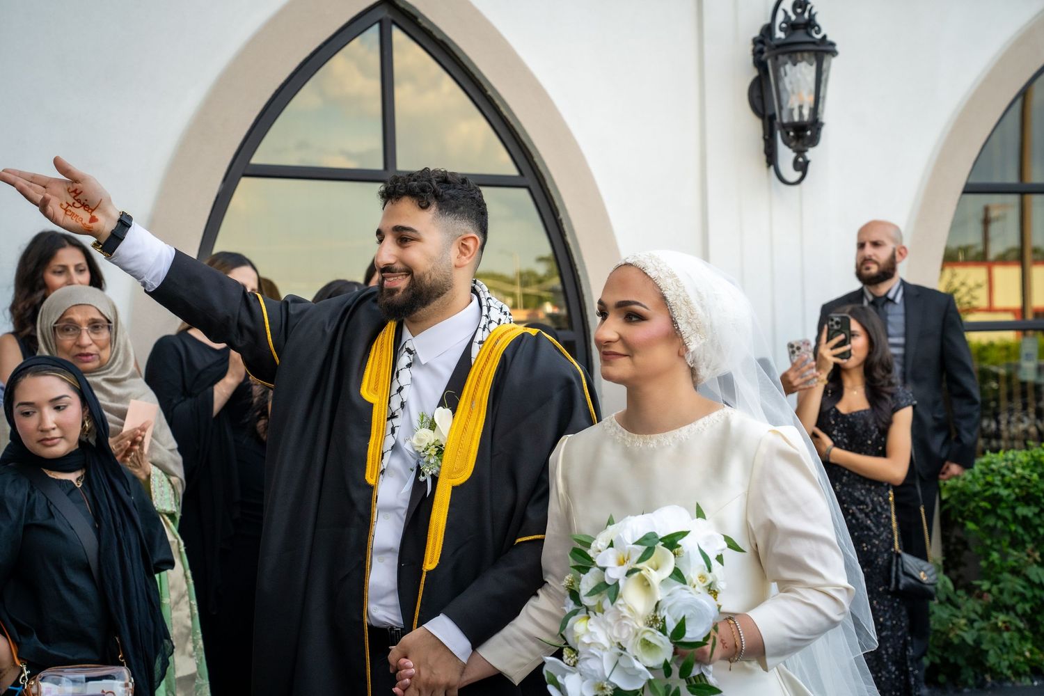 Wedding celebration outside an arched entrance with traditional cultural attire.
