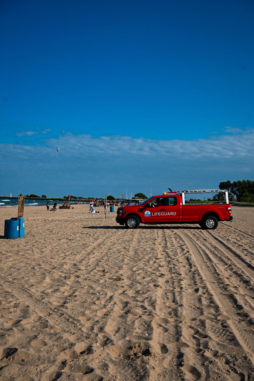 Red lifeguard truck parked on a sandy beach with blue sky overhead.