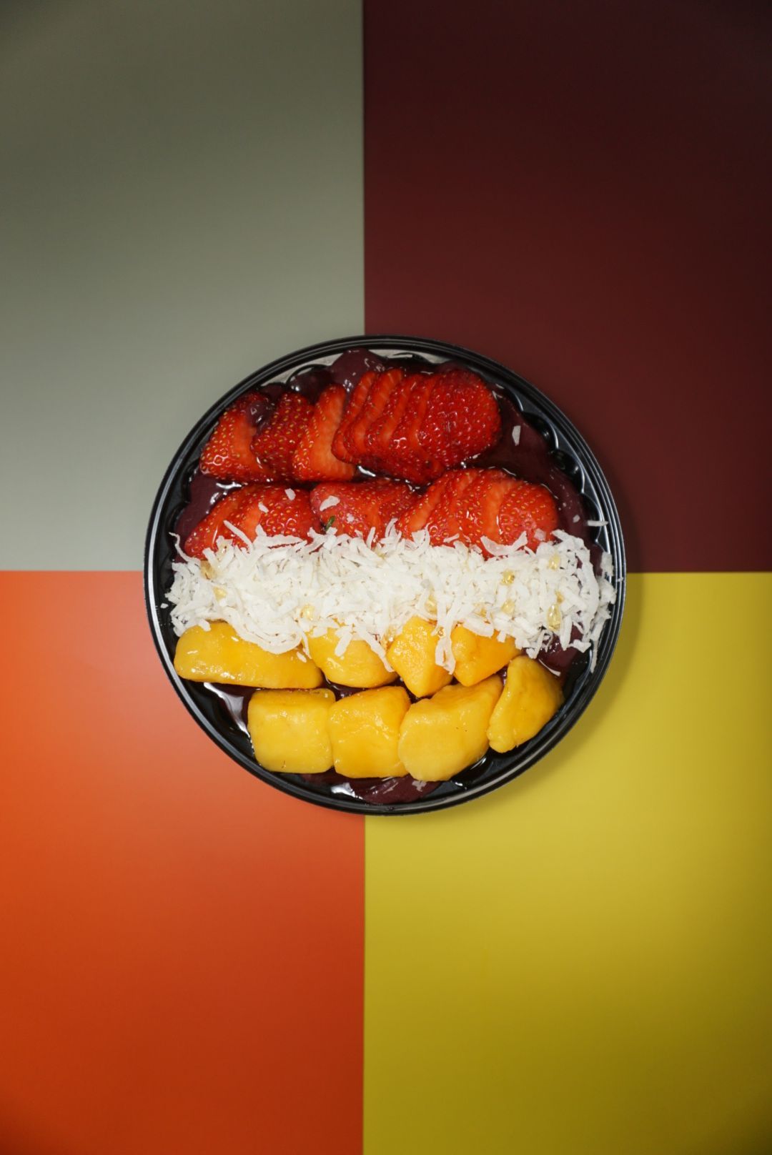 Fresh mango and strawberry dessert plated on black dish with shredded coconut.