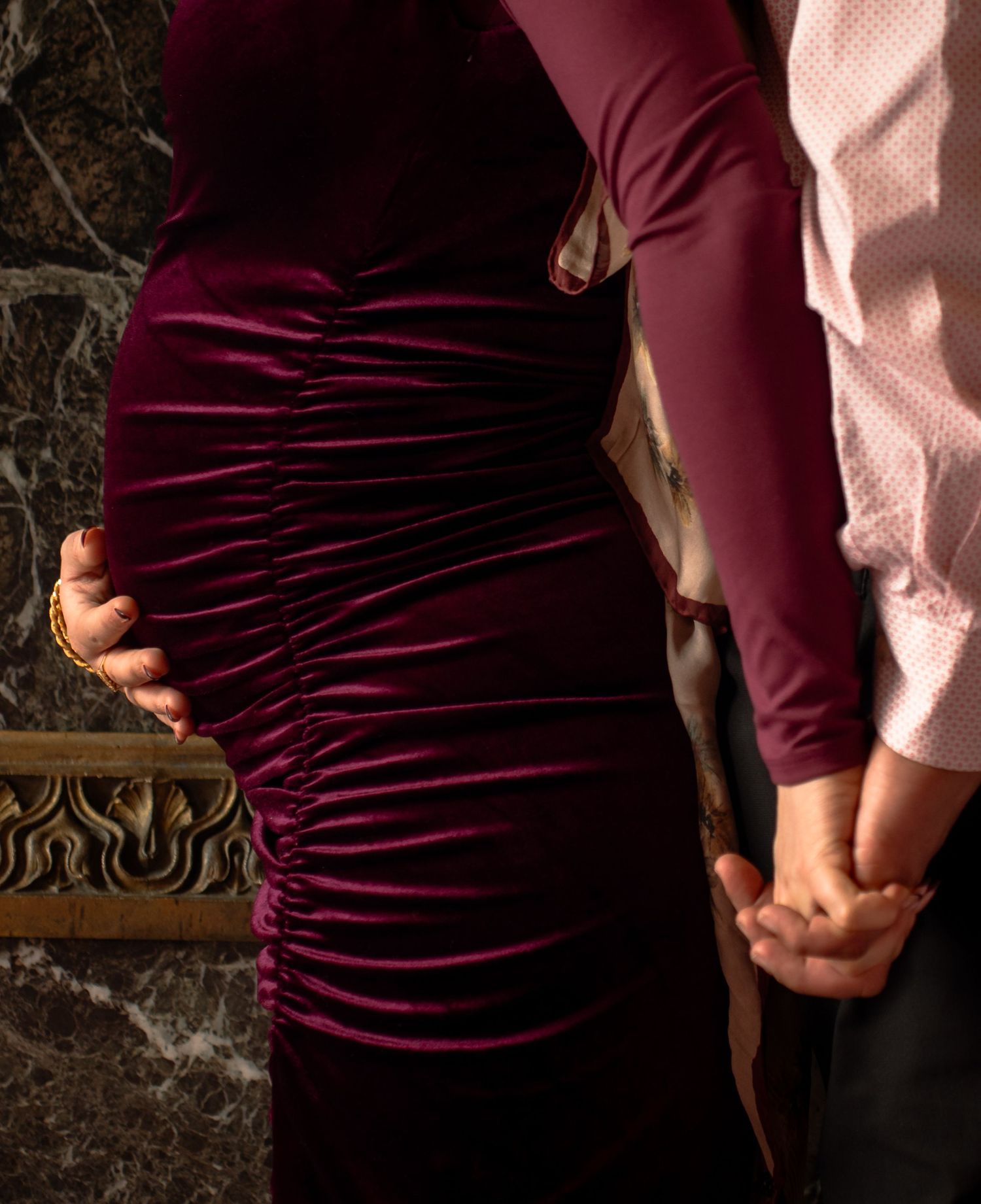 A couple wearing burgundy and pink outfits holds hands in a romantic engagement photo session.