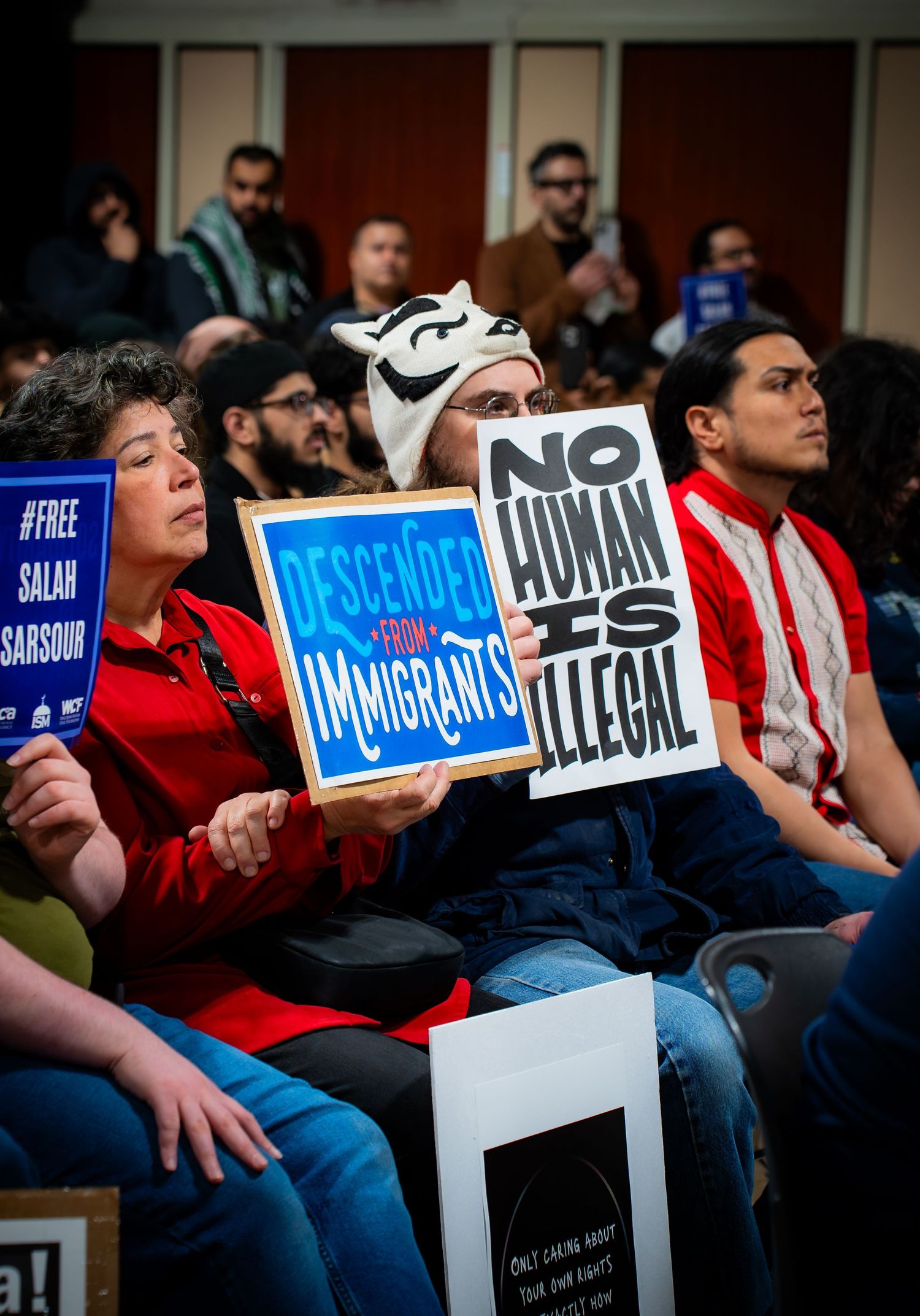 Protesters at rally holding signs reading 'No Human Is Illegal' and 'Descended From Immigrants' advocating for immigrant rights.