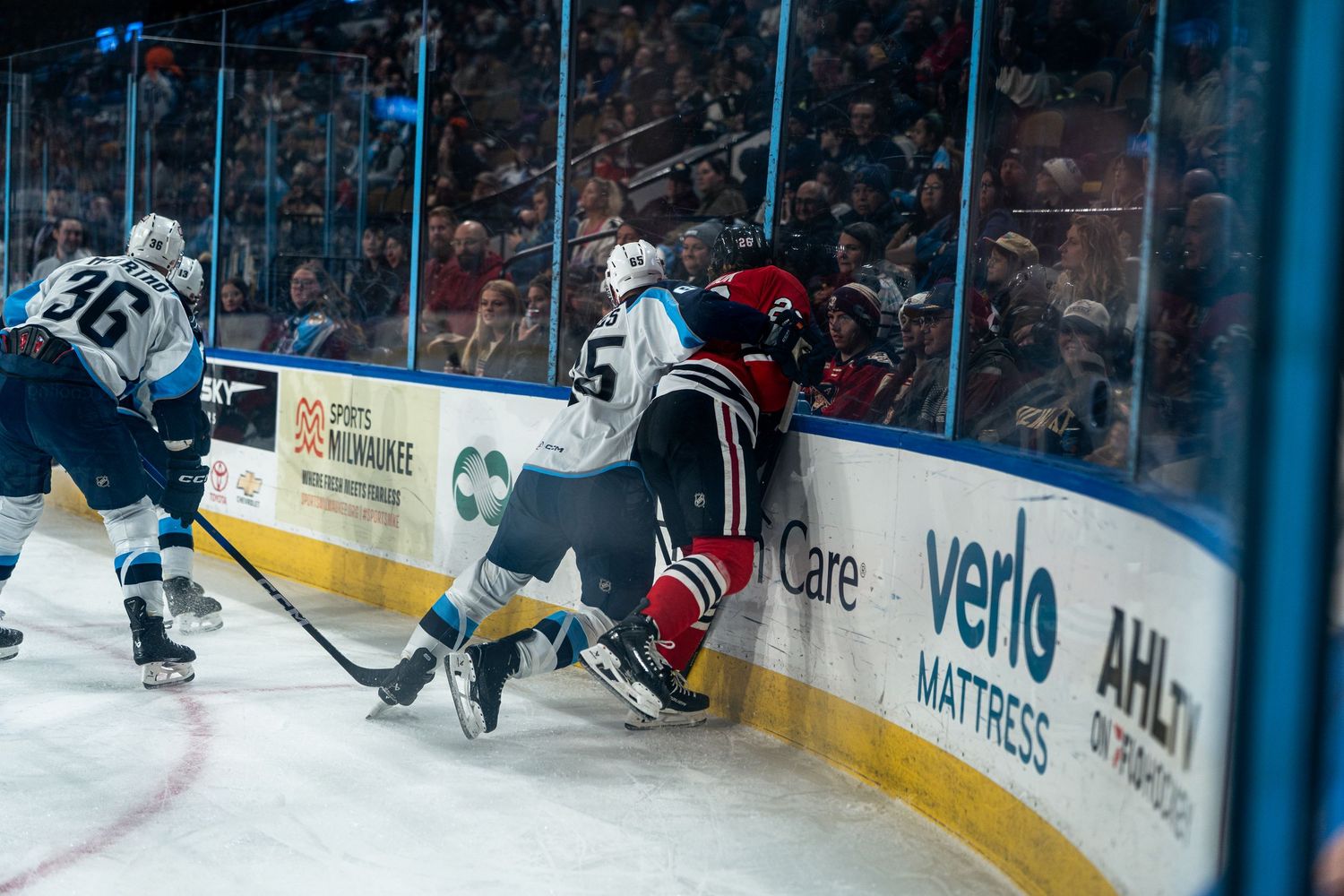 Hockey players battle for position near the boards during intense game action.