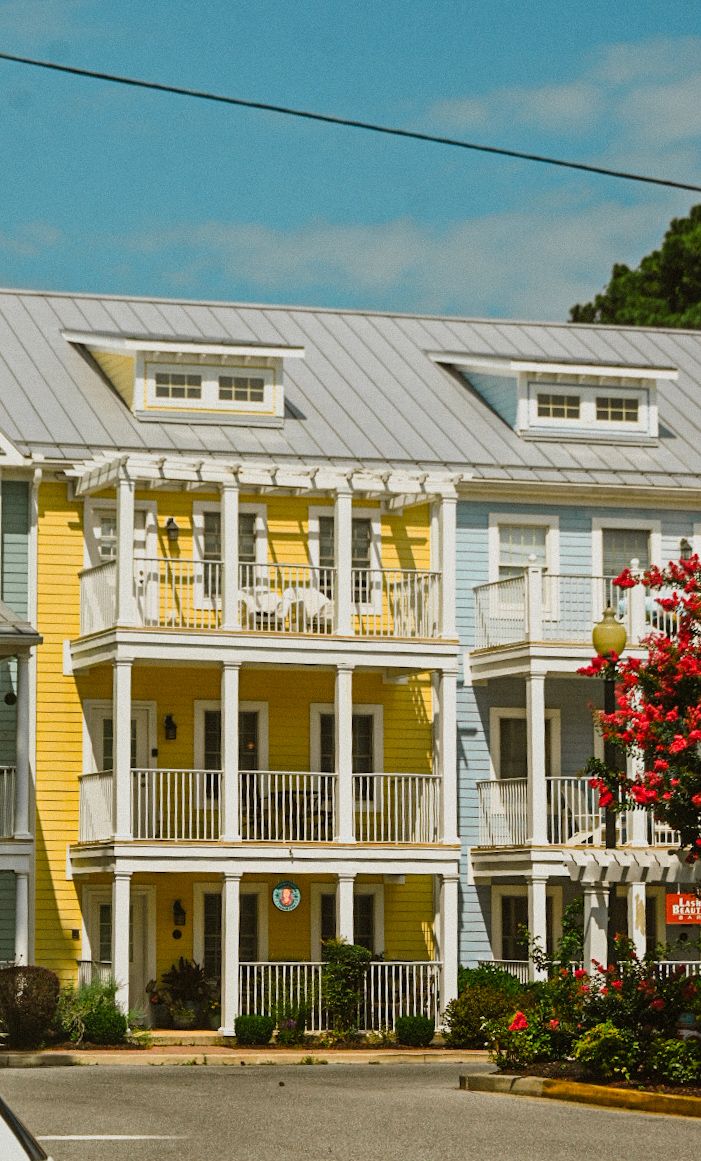 Row of yellow and white coastal homes with wraparound porches and metal roofs.