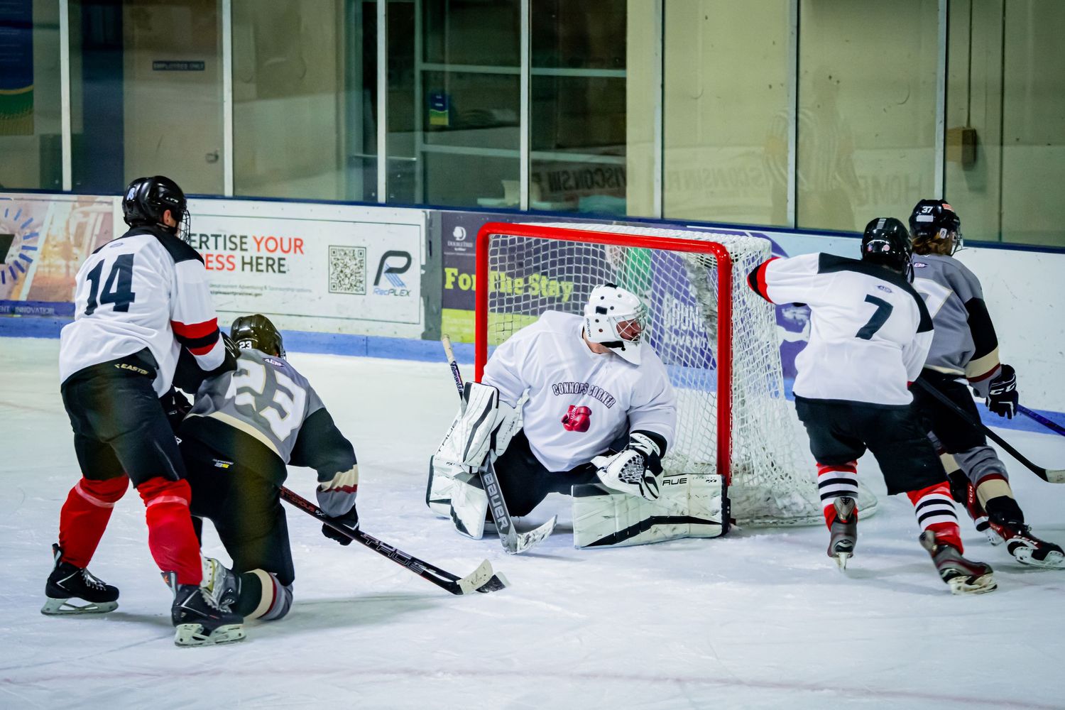Intense hockey action near the goal with multiple players battling for position.