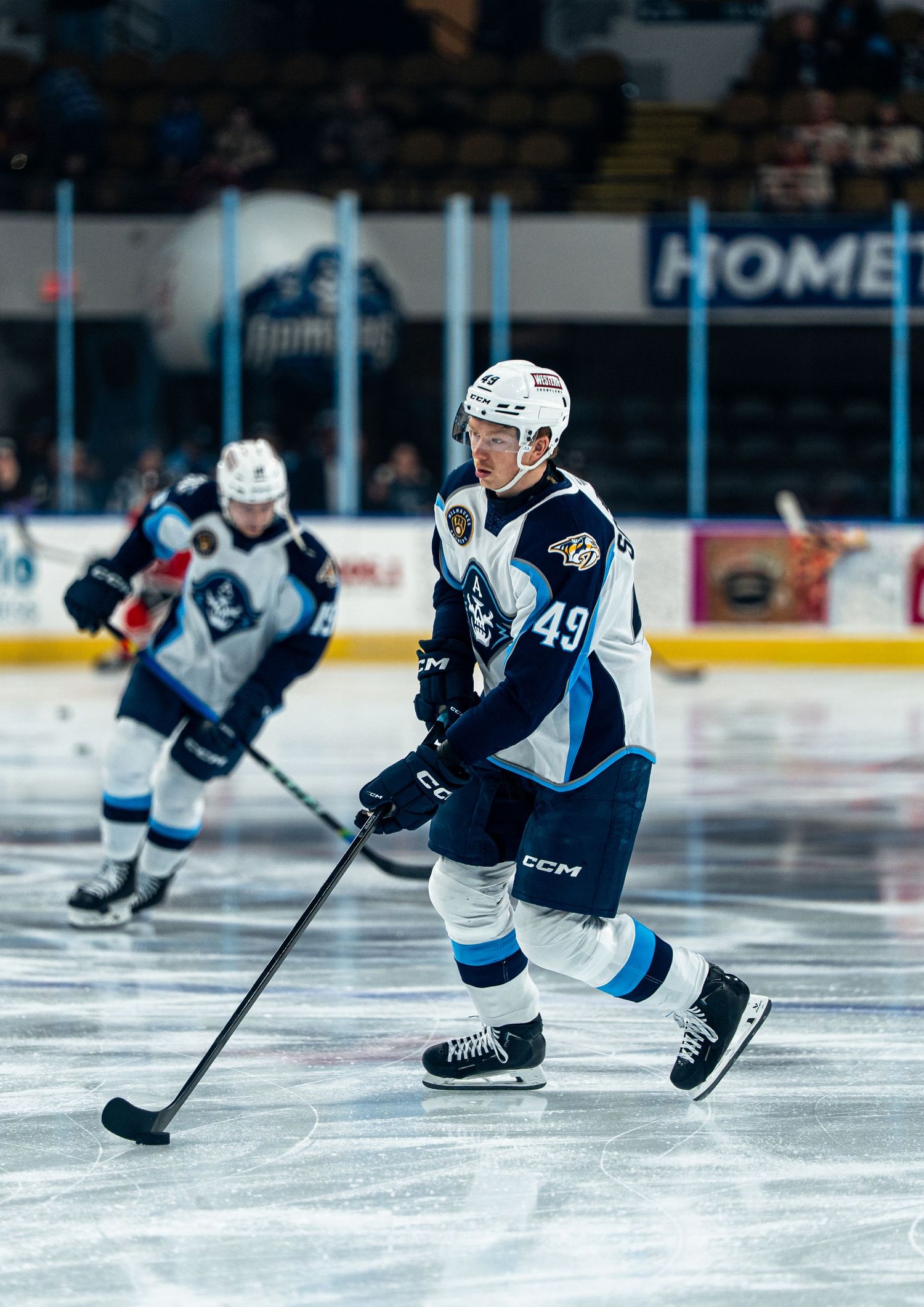 Hockey player in dark blue jersey skates across ice during game action.