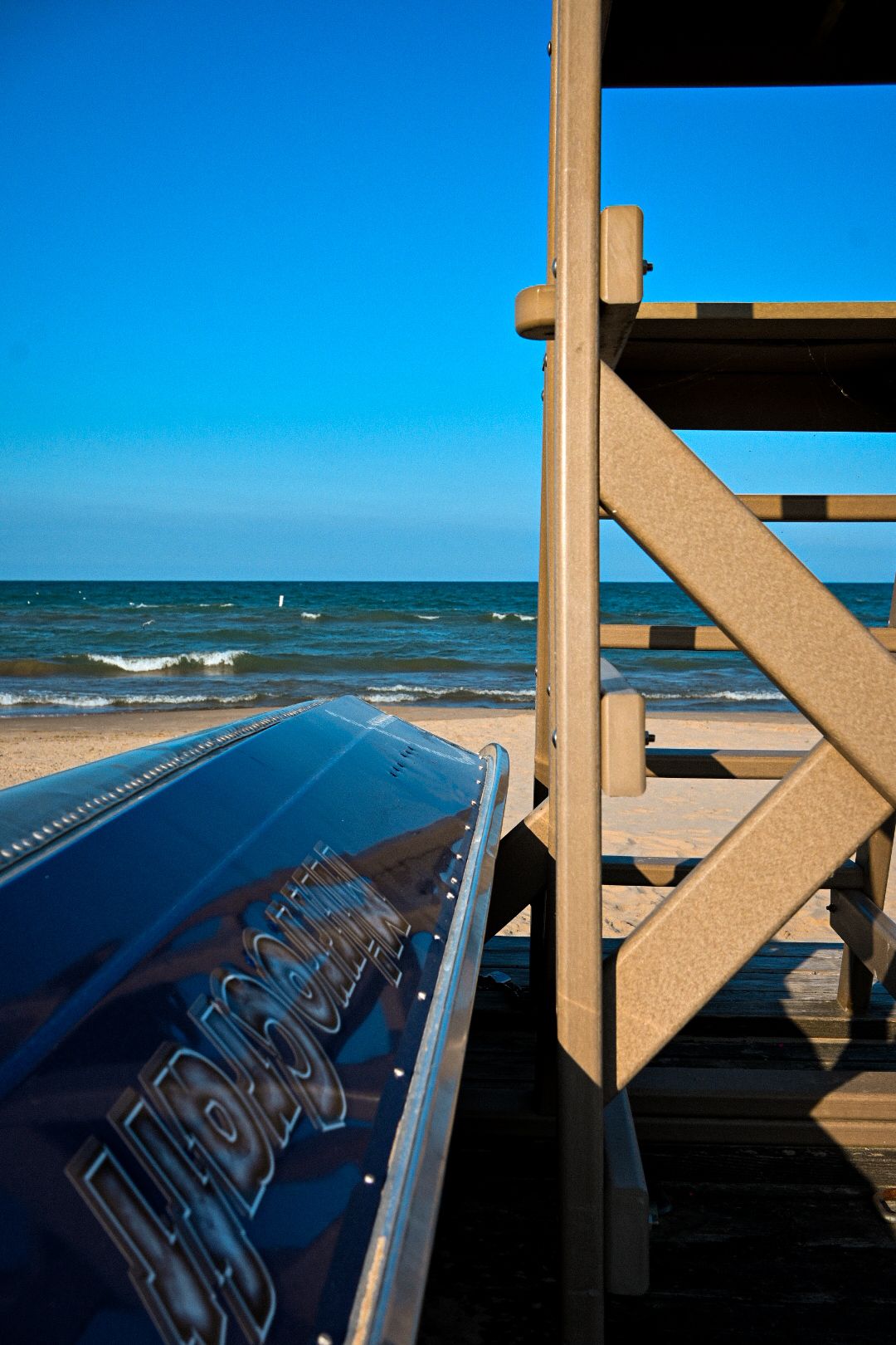 Lifeguard tower steps overlooking ocean waves under bright blue sky.