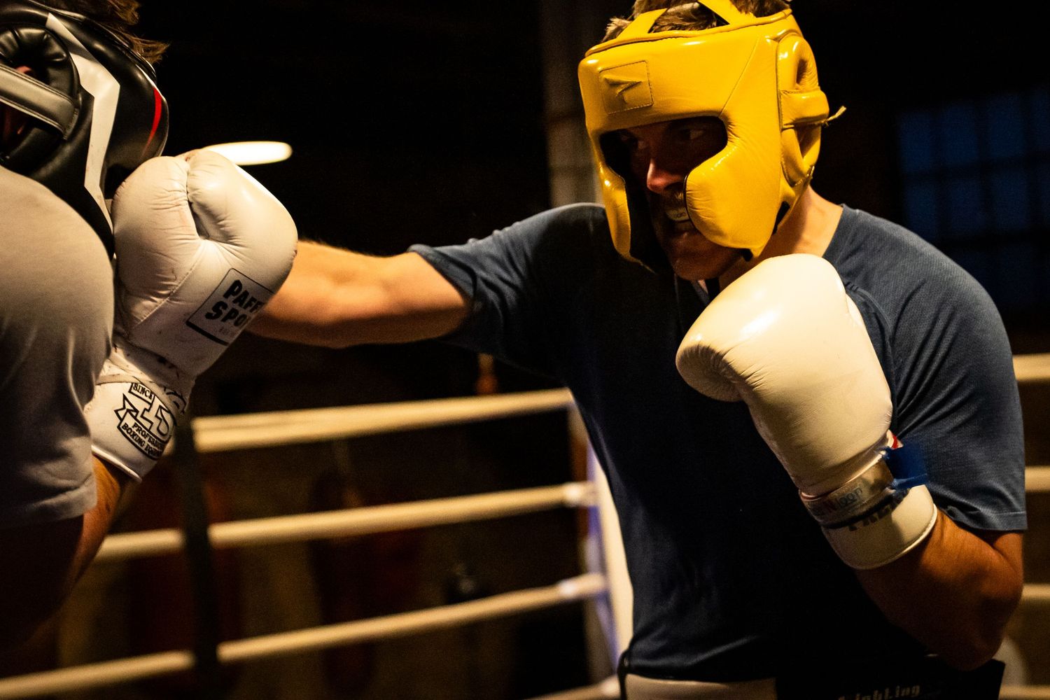 Boxers wearing protective headgear exchange punches during training session.