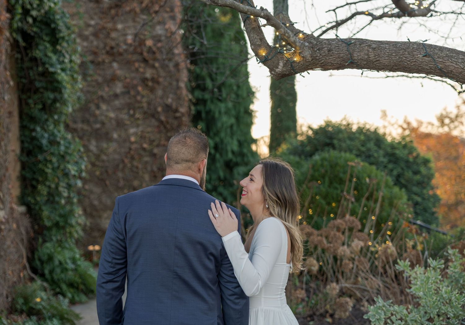 Couple sharing a romantic moment in a lush garden setting, man in blue suit and woman in white dress.