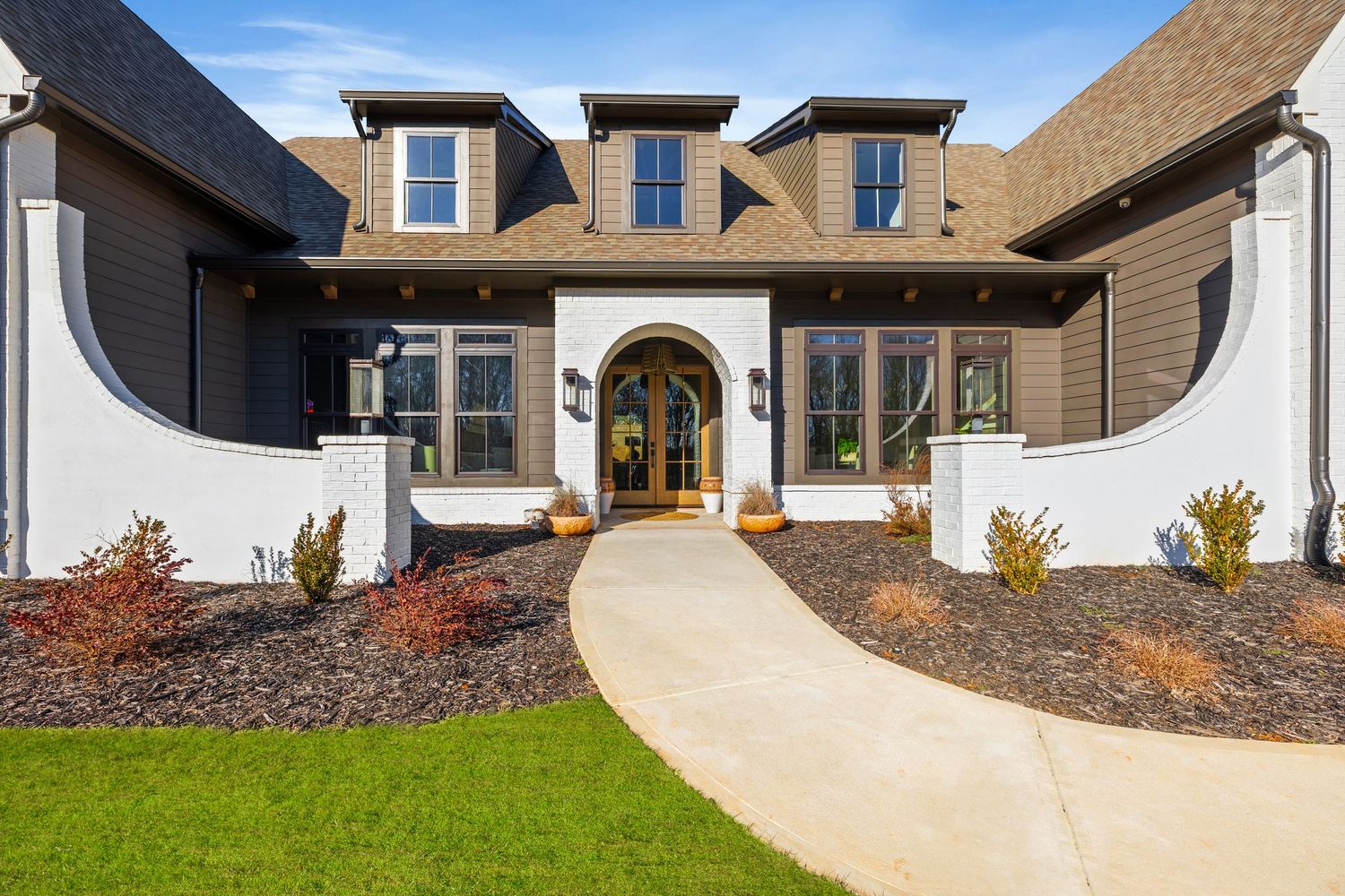Elegant craftsman-style home with arched entry, white columns, curved walkway, and manicured landscaping.