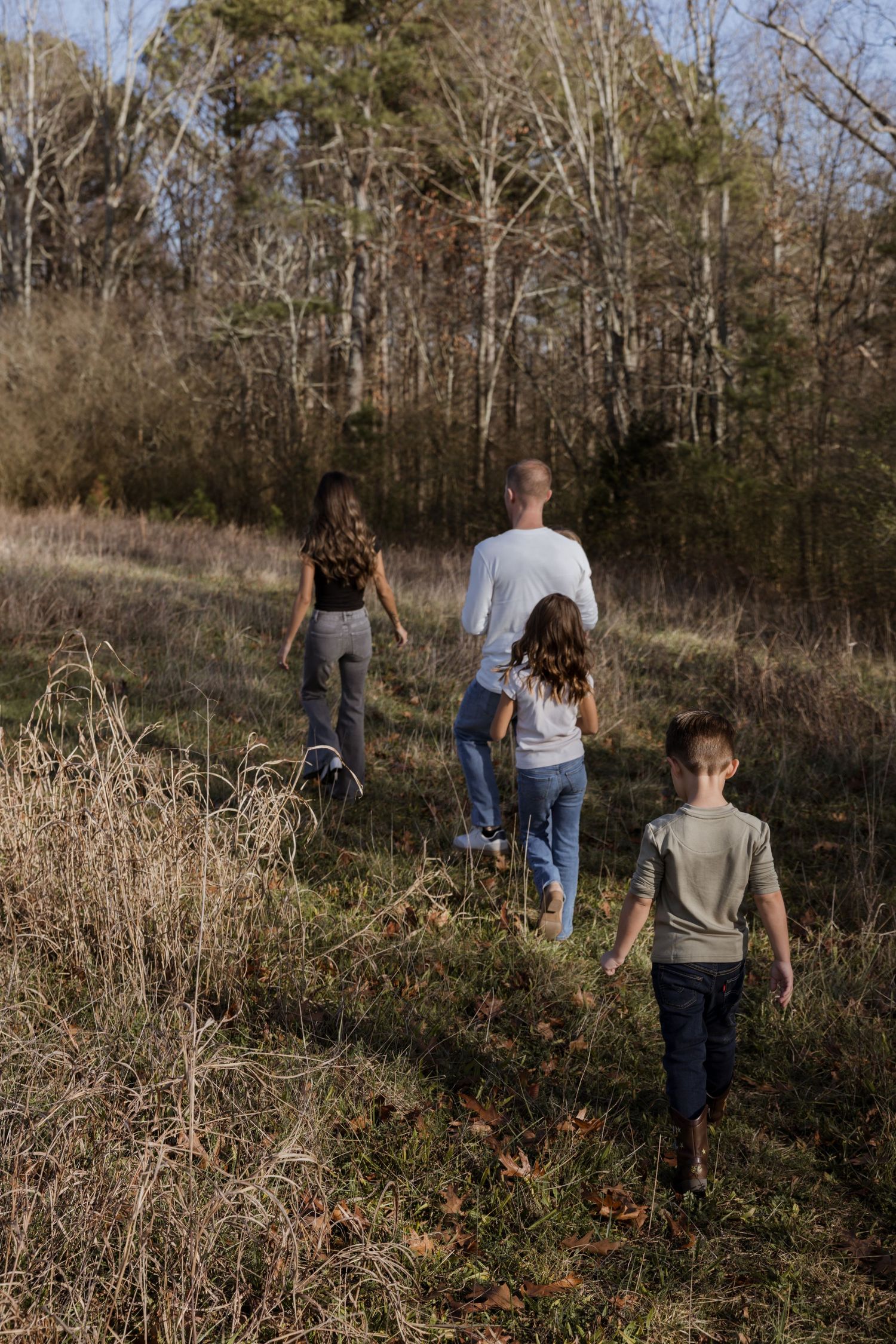 Family of four walking through an open field toward a forest on a sunny autumn day.