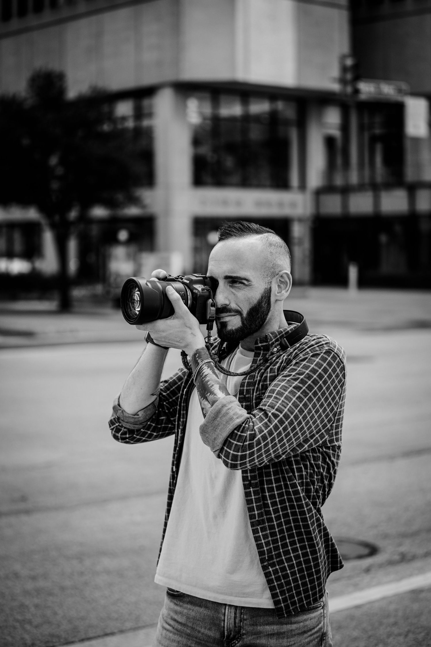 Black and white photo of photographer shooting with telephoto lens in city setting.
