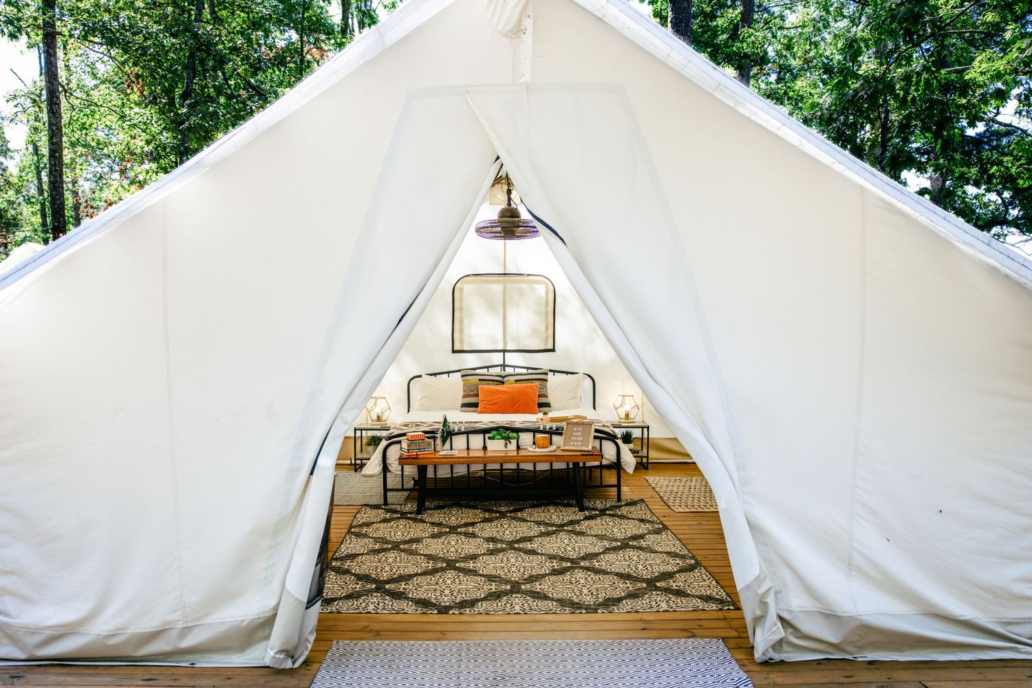 Luxury glamping bell tent with white canvas walls, a cozy bed, patterned rug, and warm lighting surrounded by trees.