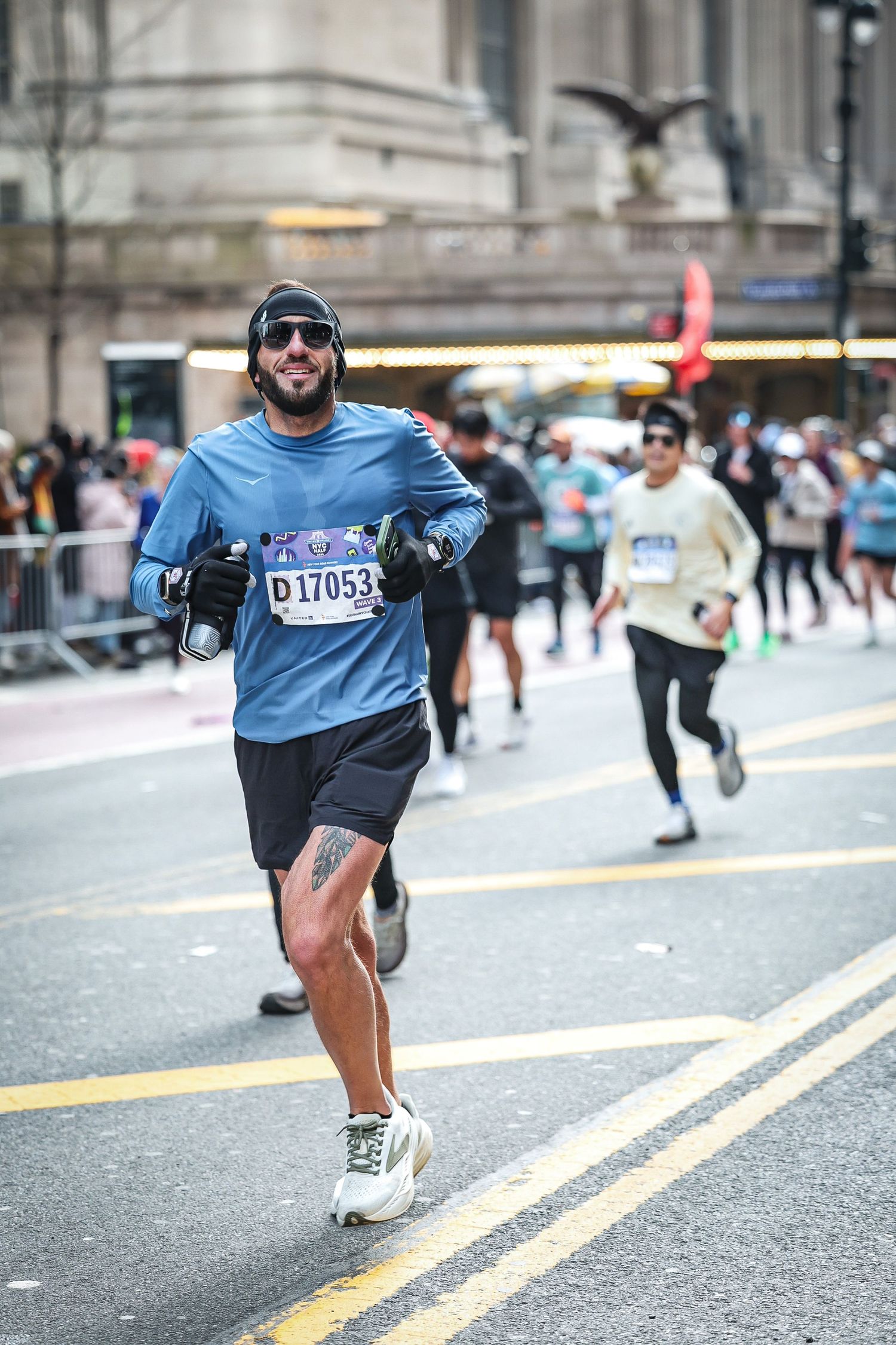 Runner races through city streets during a marathon, smiling in blue shirt and sunglasses.
